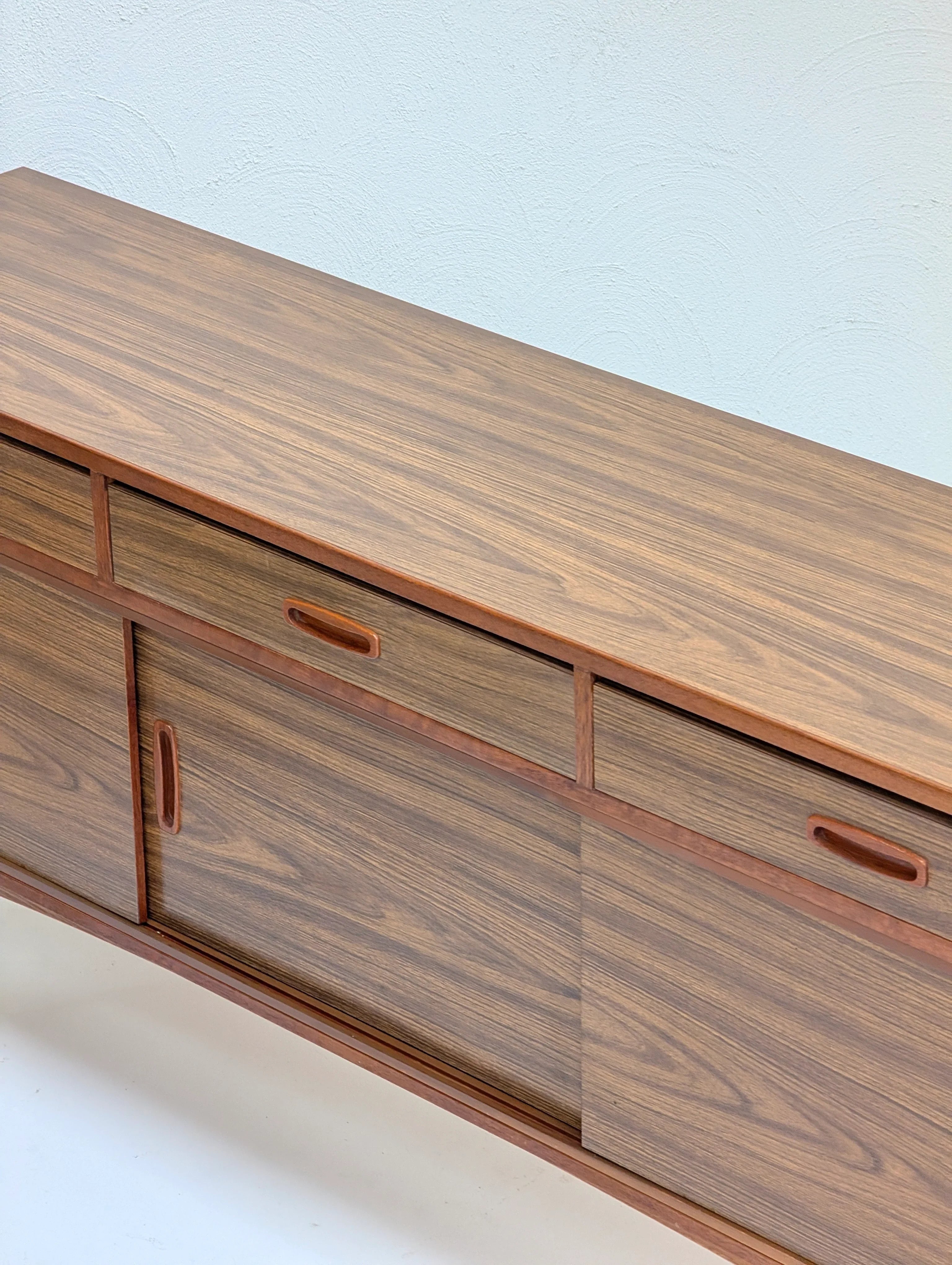 Wooden sideboard with sliding doors and drawers in a minimalist room with white walls and floor
