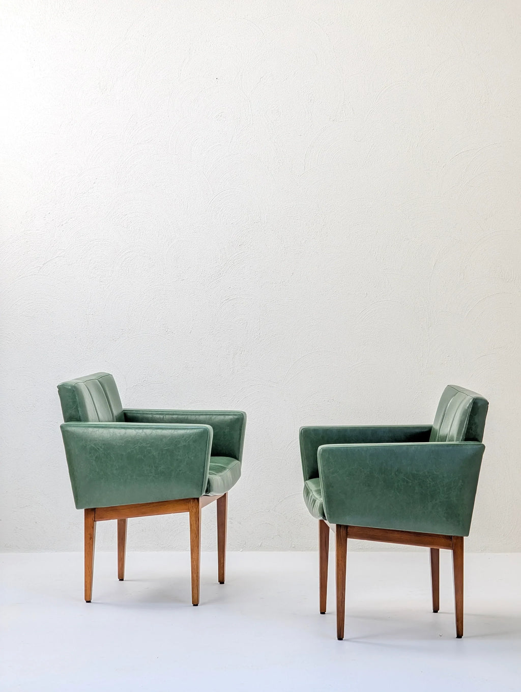 Pair of green mid-century modern armchairs with wooden legs against a white wall