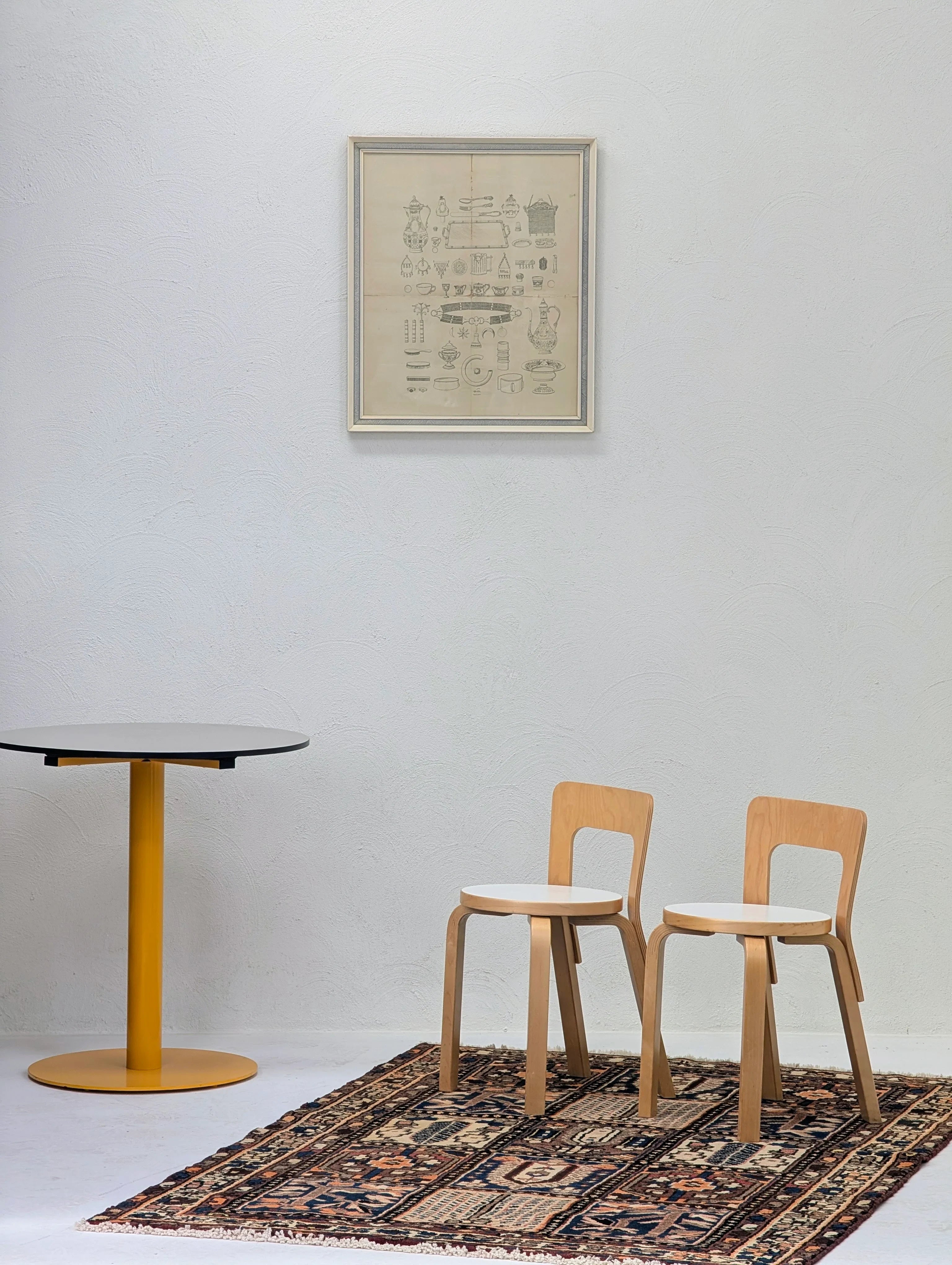 Minimalist room with two wooden chairs on patterned rug, round table with yellow base, and framed vintage art