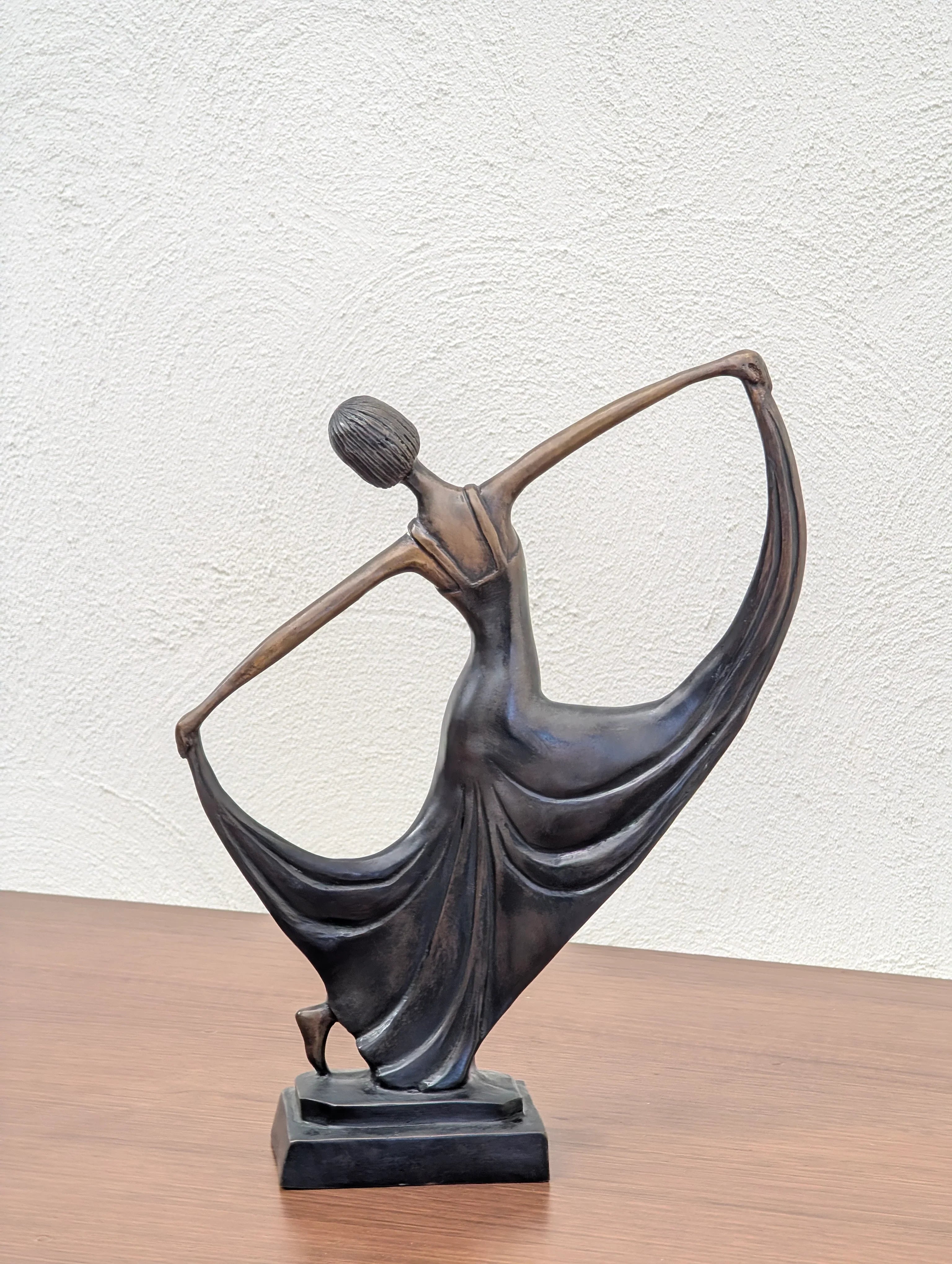Bronze sculpture of a female dancer gracefully holding her flowing dress on wood surface