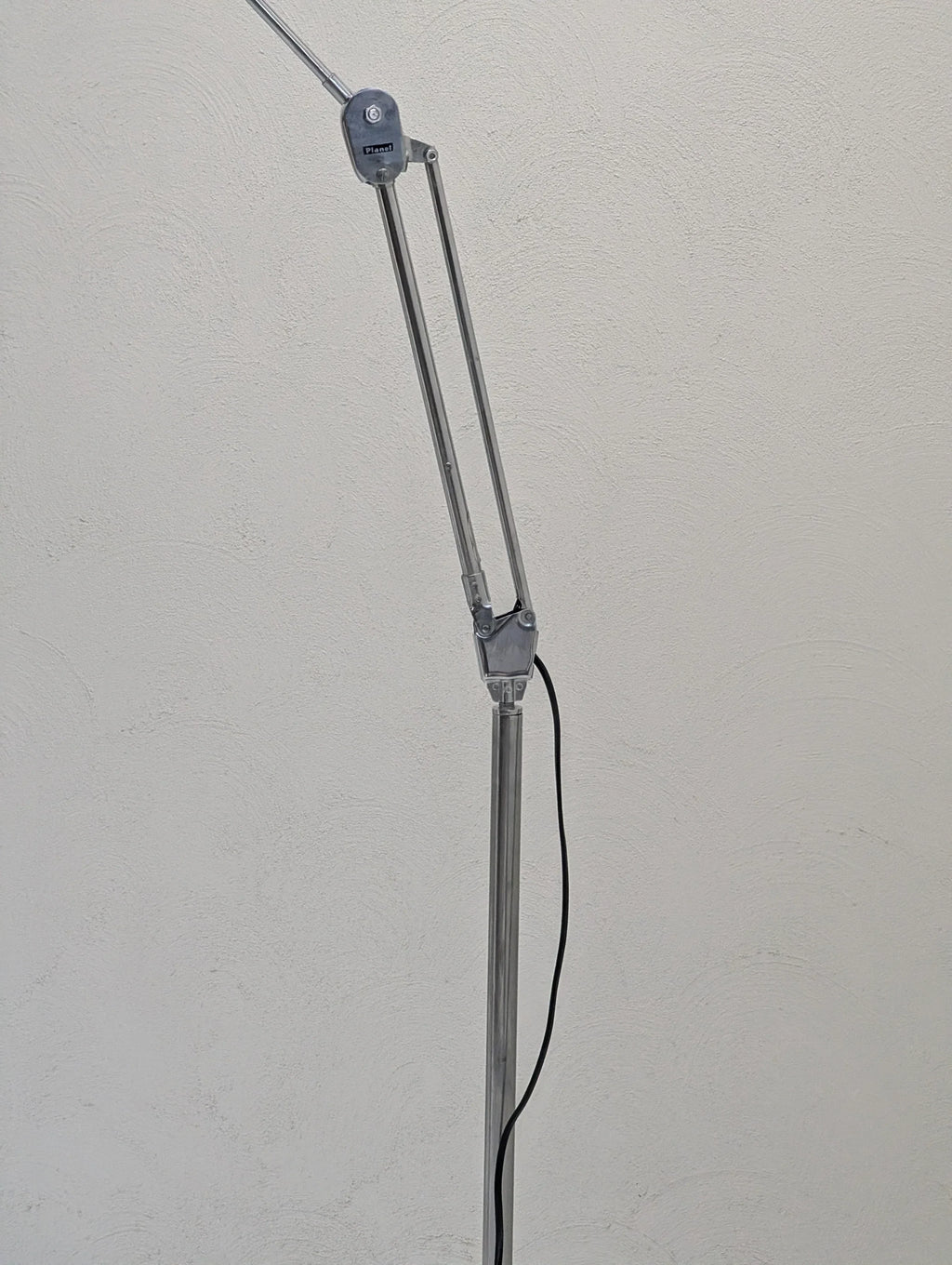 Adjustable silver task lamp with black power cord against a textured white wall.