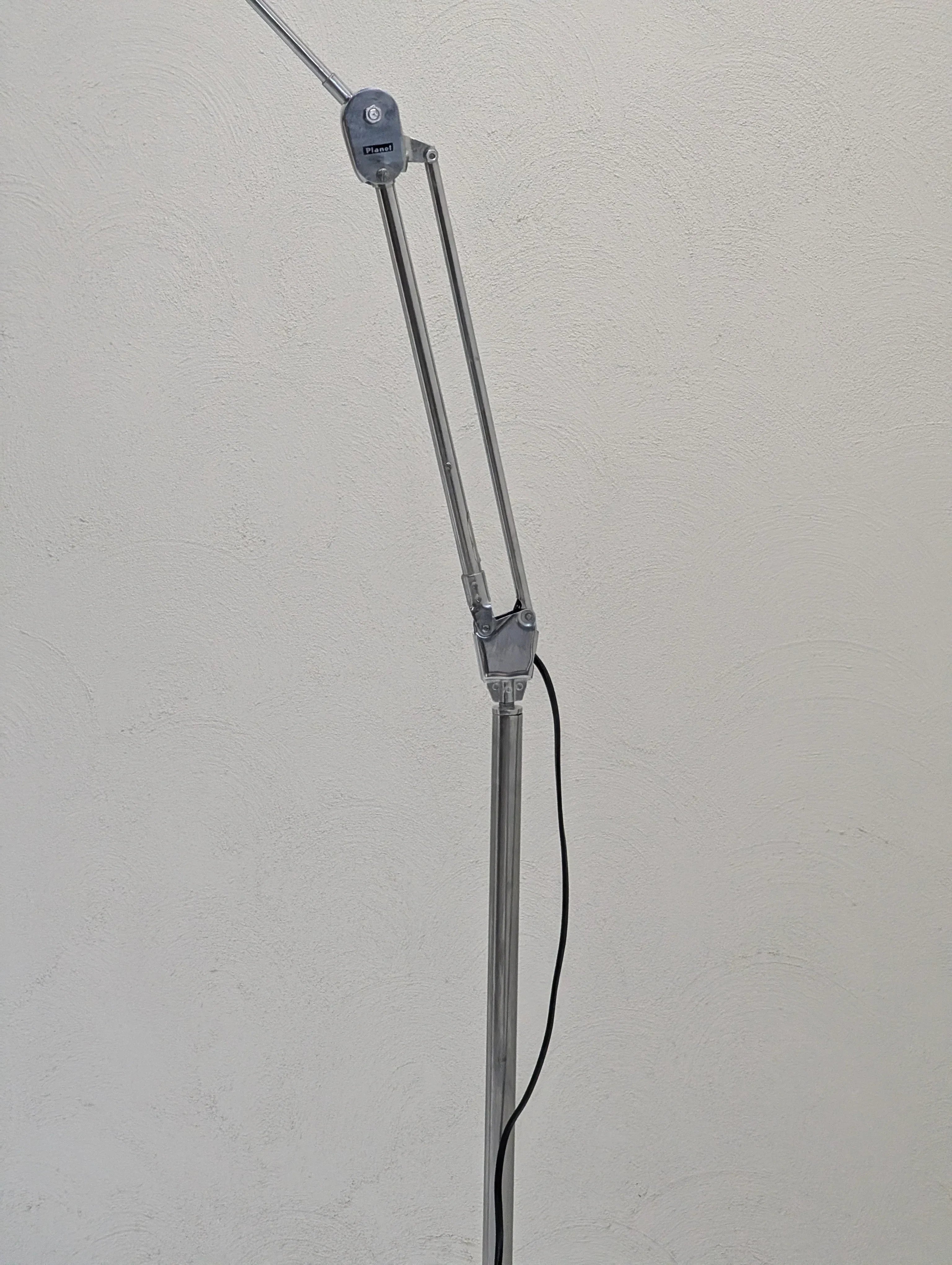 Adjustable silver task lamp with black power cord against a textured white wall.