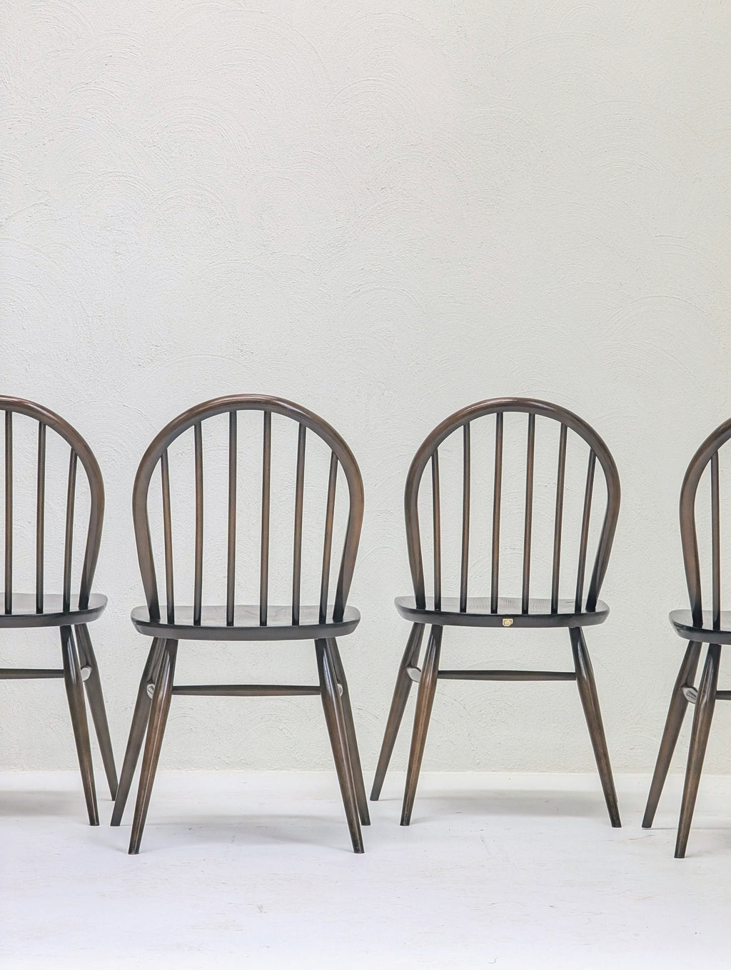 Four wooden chairs with rounded backs and spindle design against a textured white wall
