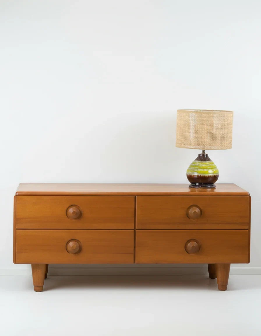 Mid-century modern wooden dresser with four drawers and a ceramic table lamp