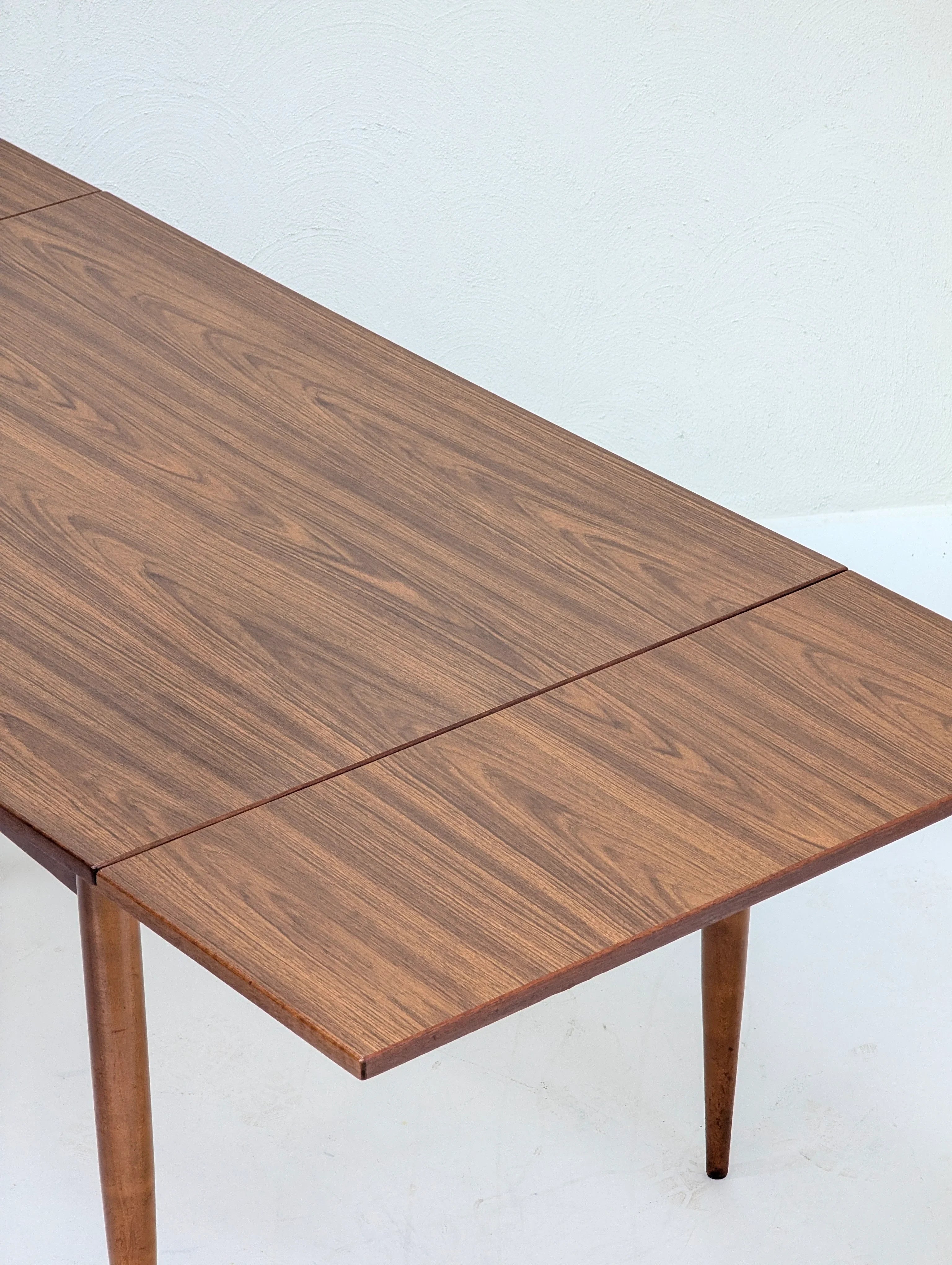 Mid-century modern wooden dining table with leaf extension and tapered legs on white floor