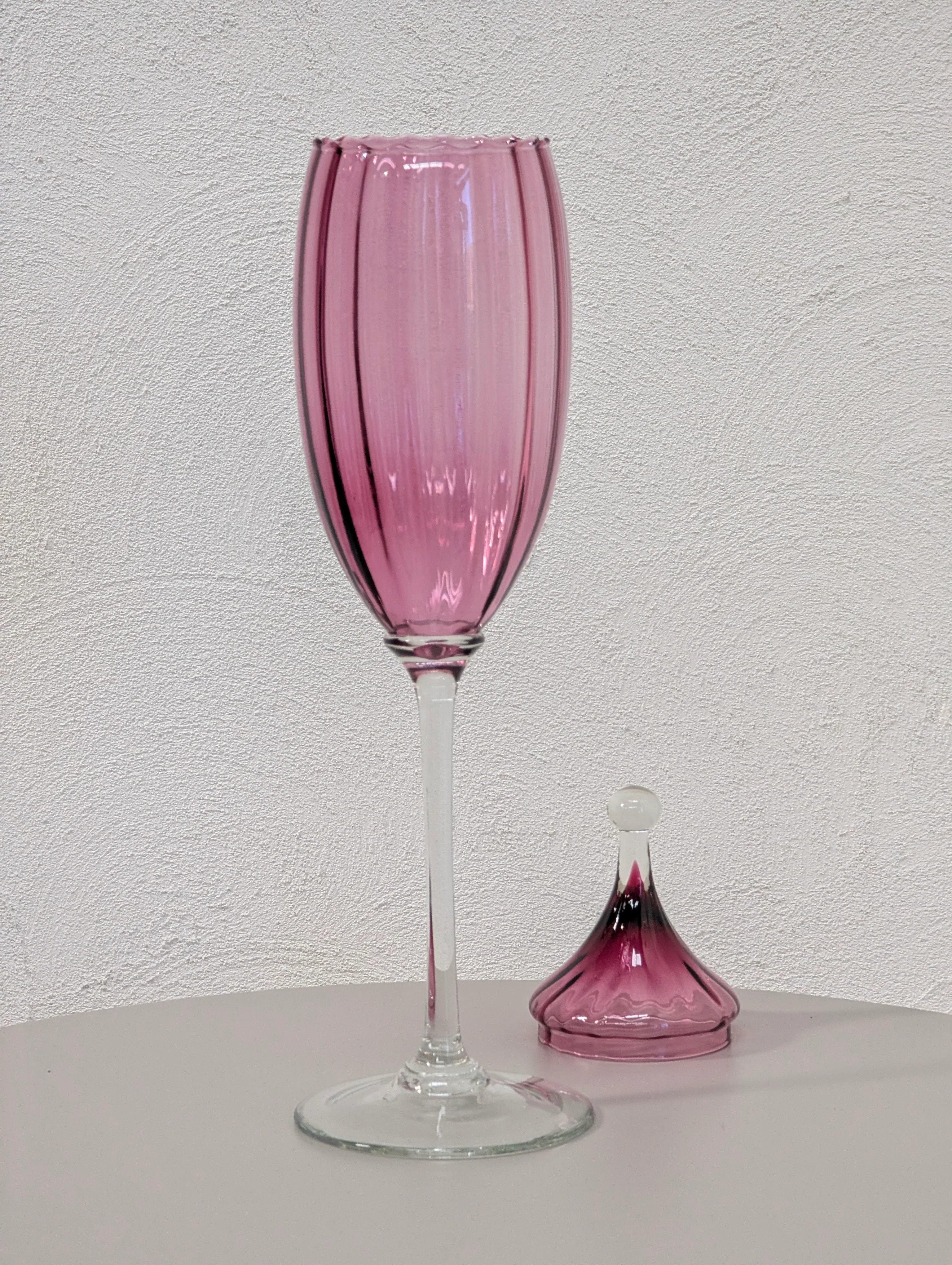 Tall pink vintage glass with clear stem next to matching glass stopper on white table