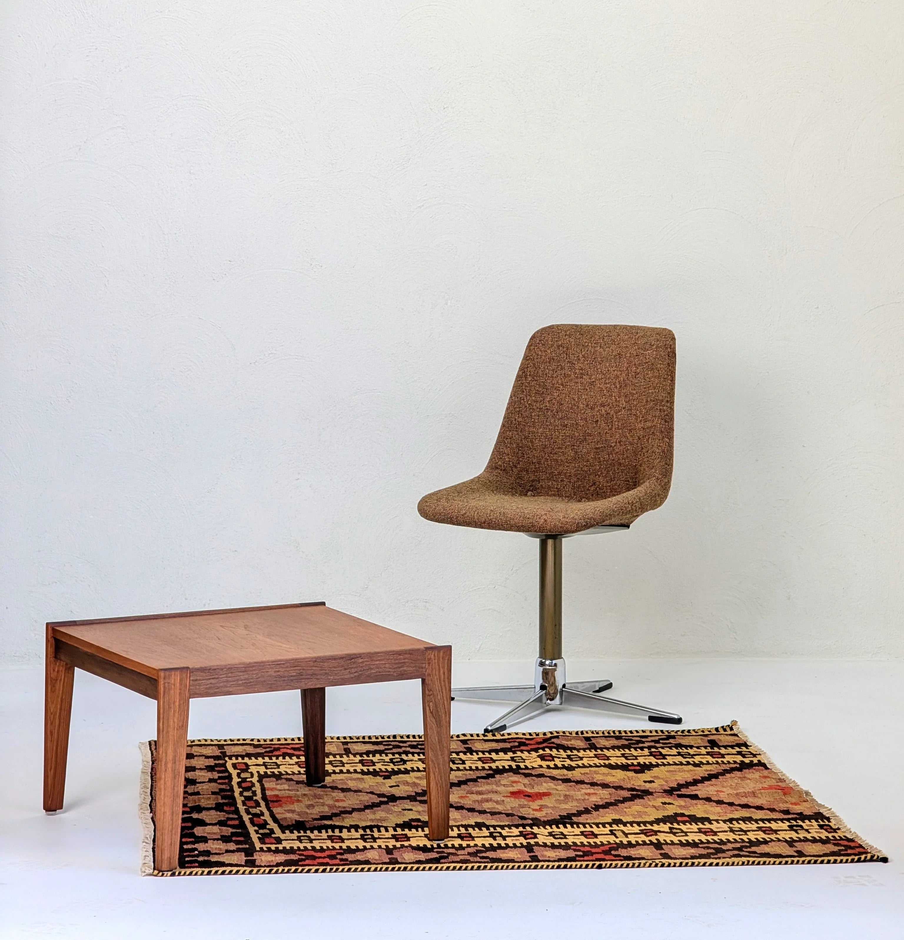 Brown fabric swivel chair and wooden coffee table on patterned rug against white wall