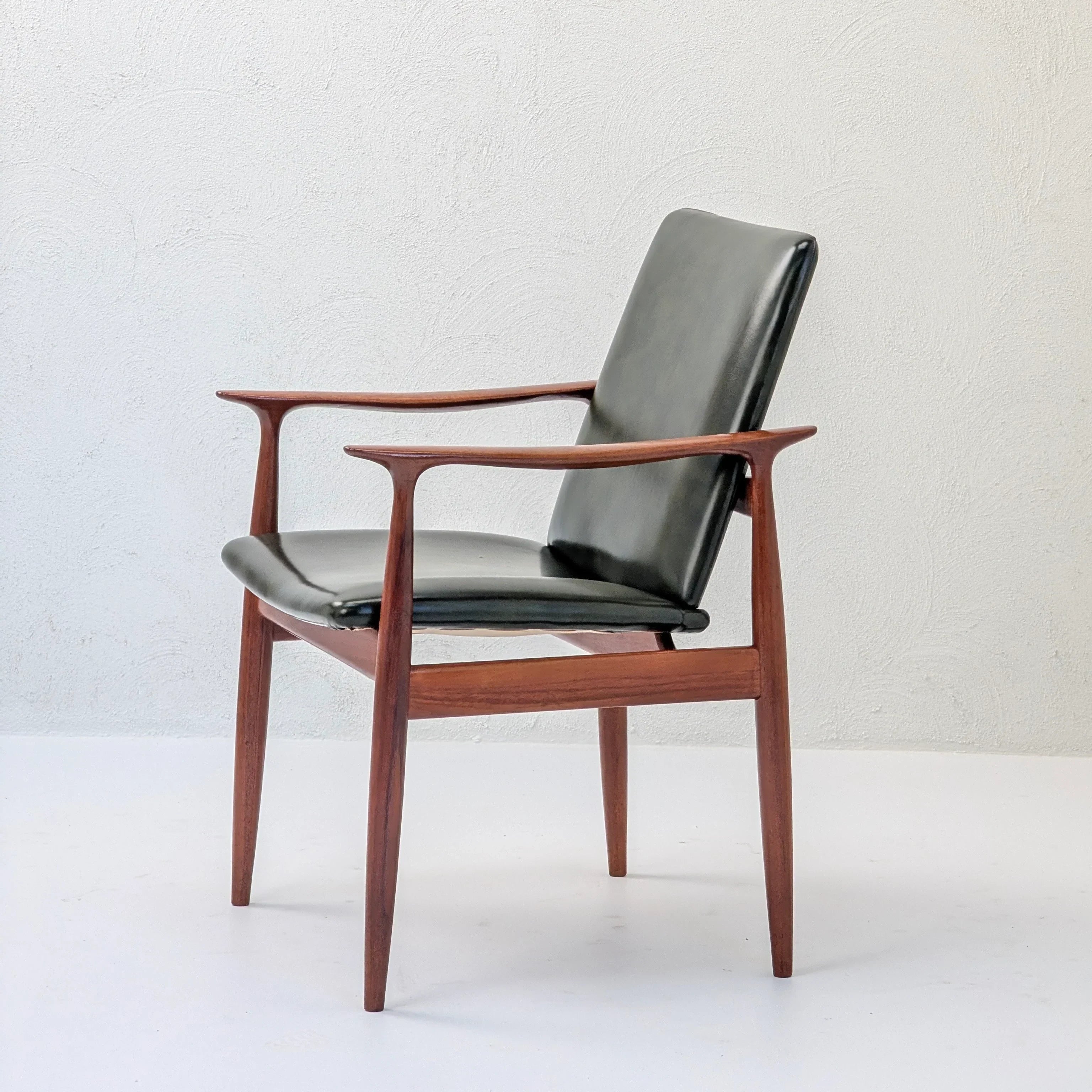 Mid-century modern wooden armchair with black leather seat and backrest on white background