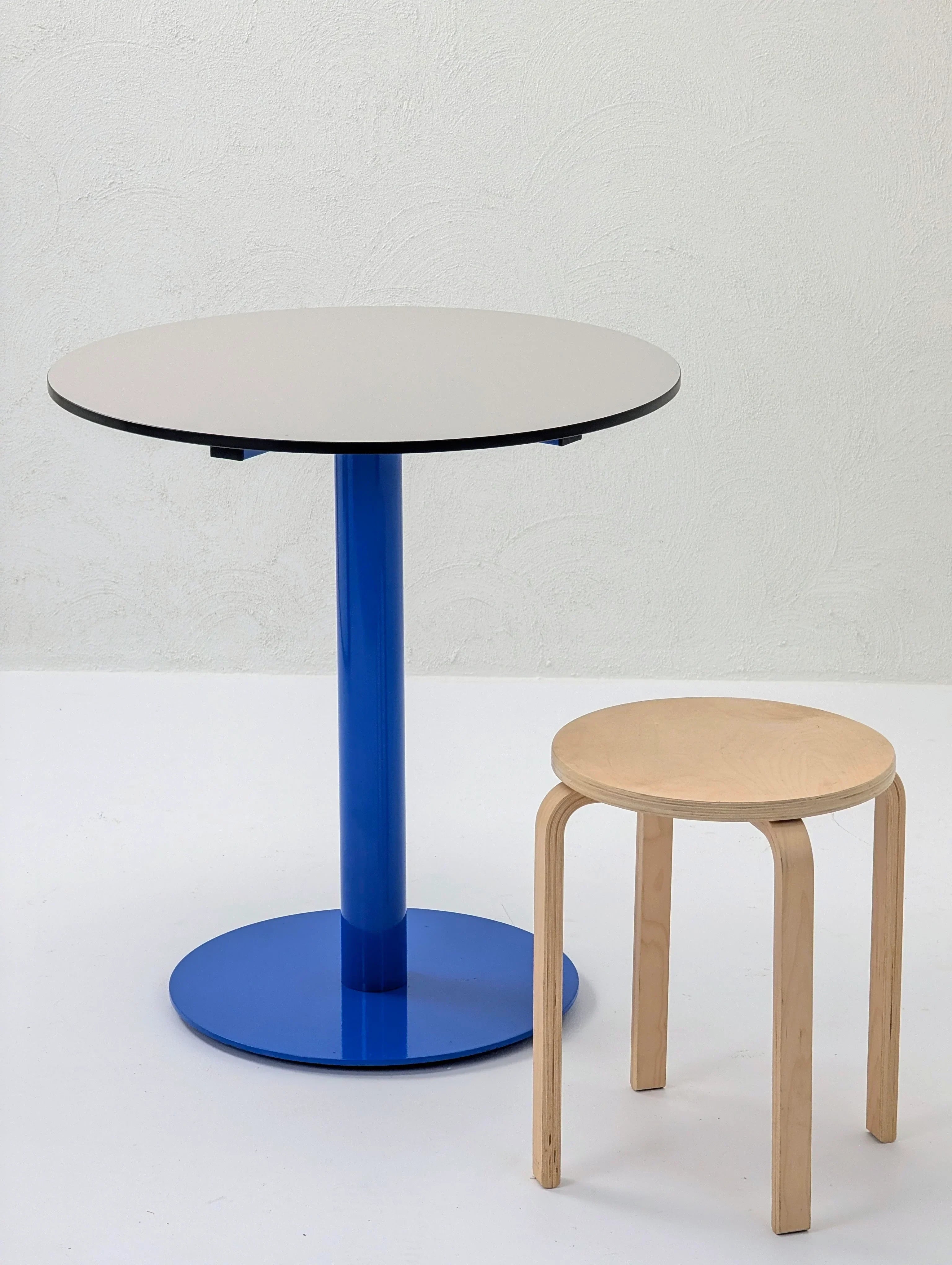 Modern blue pedestal table with round top and light wood stool on white background