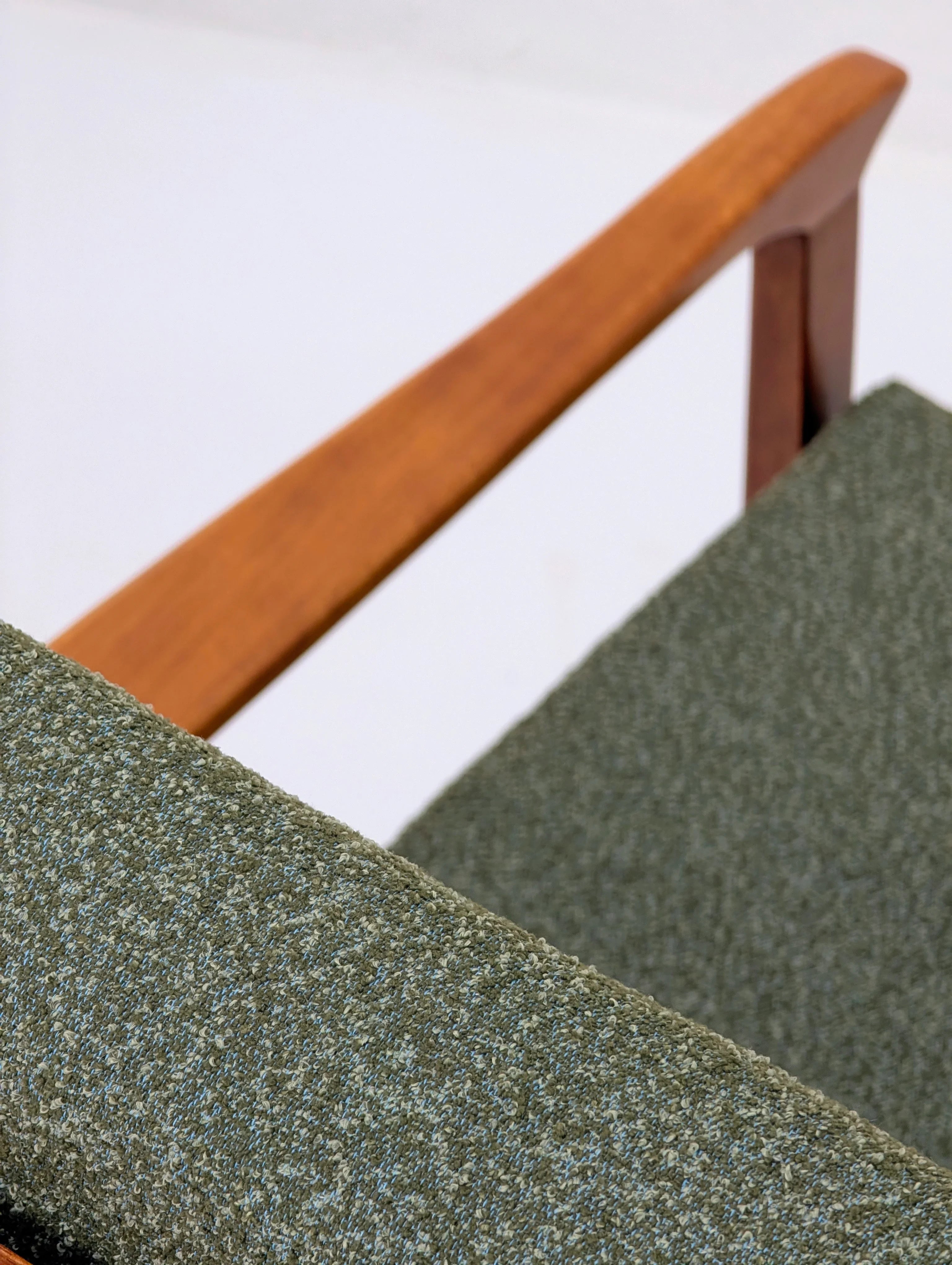 Close-up of green textured fabric chair with wooden armrest against white background