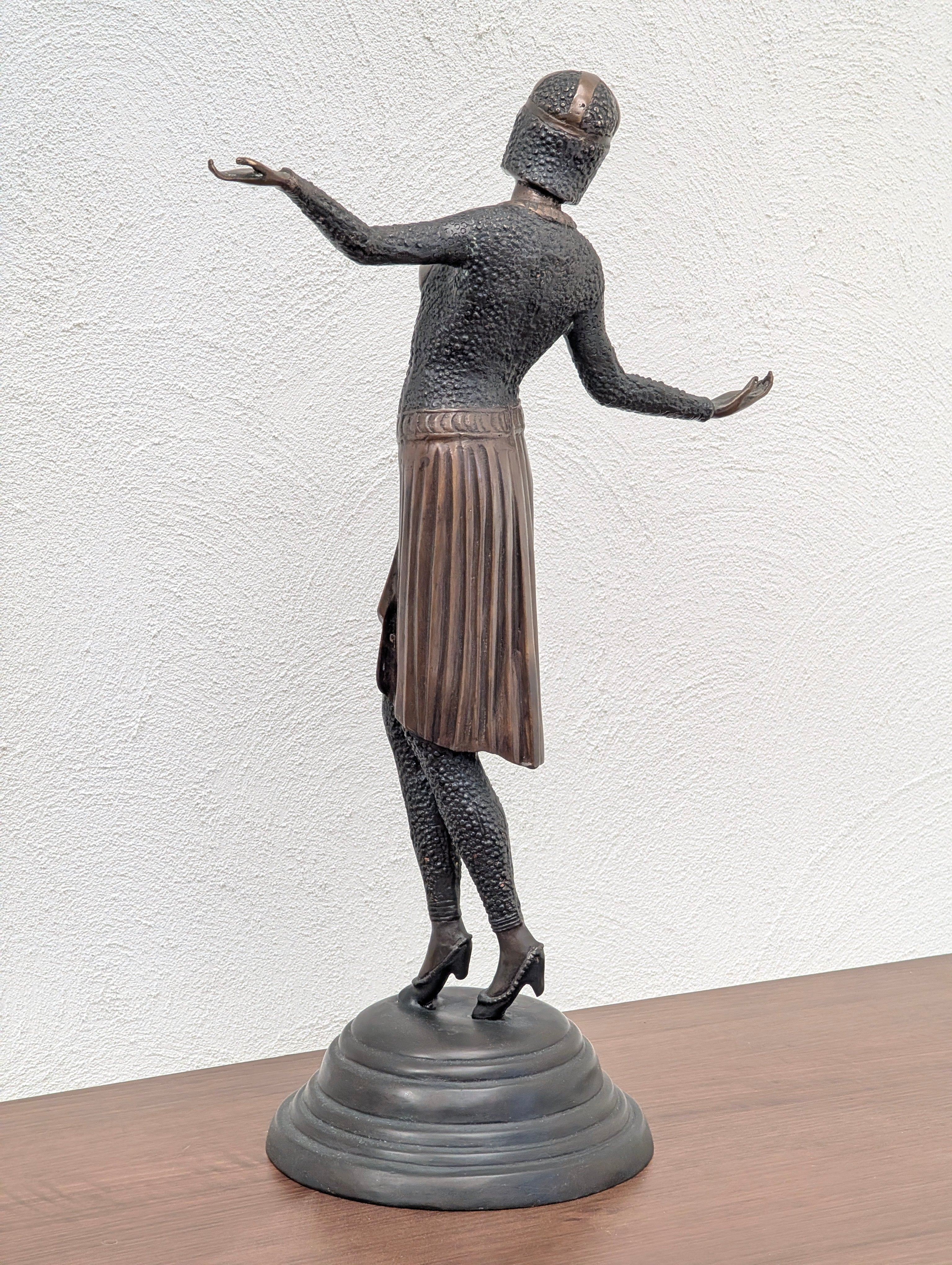 Bronze statue of a medieval armored figure in a skirt, standing on a round base against a textured white wall