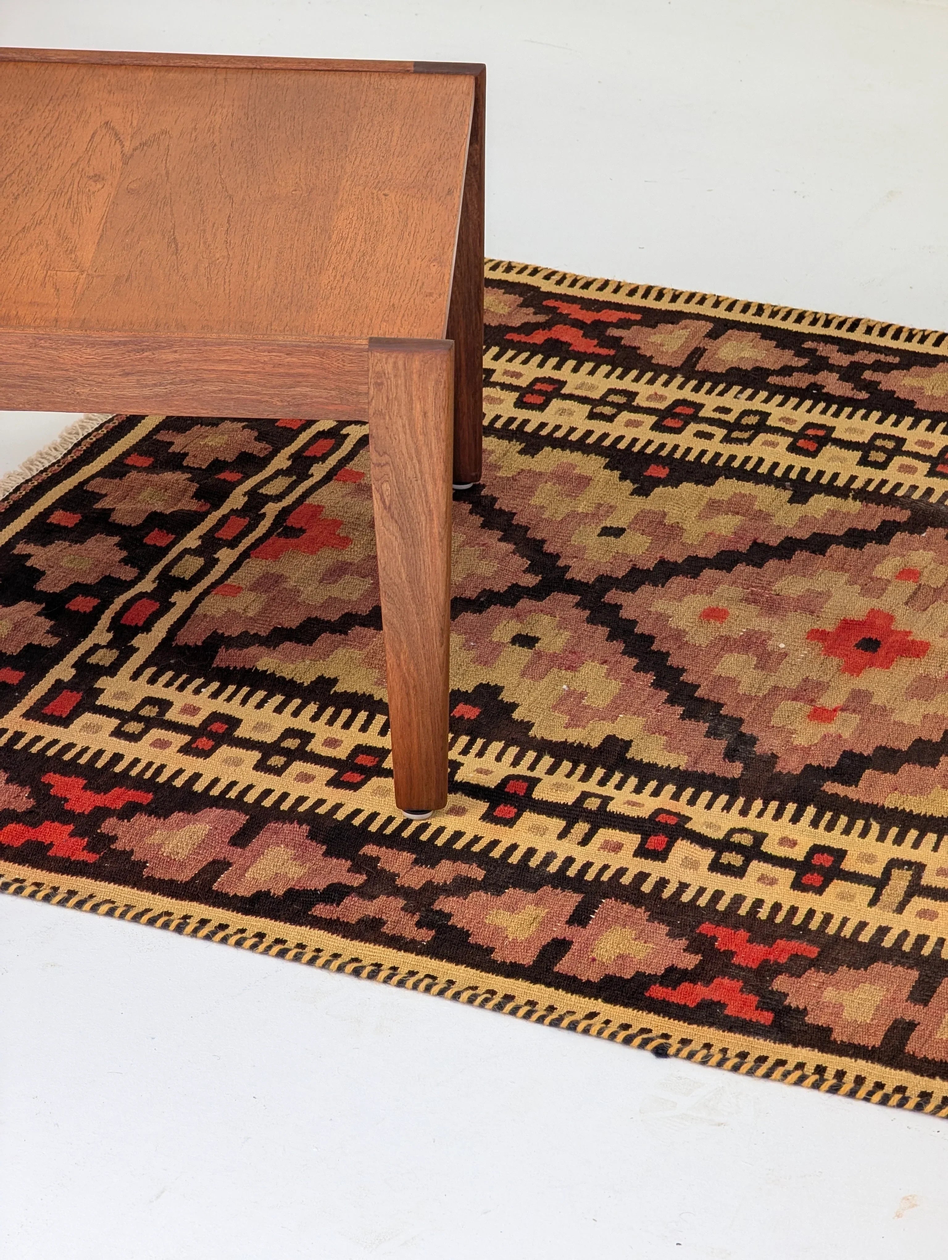 Mid-century wooden table leg on a traditional patterned rug with red, brown, and beige colors