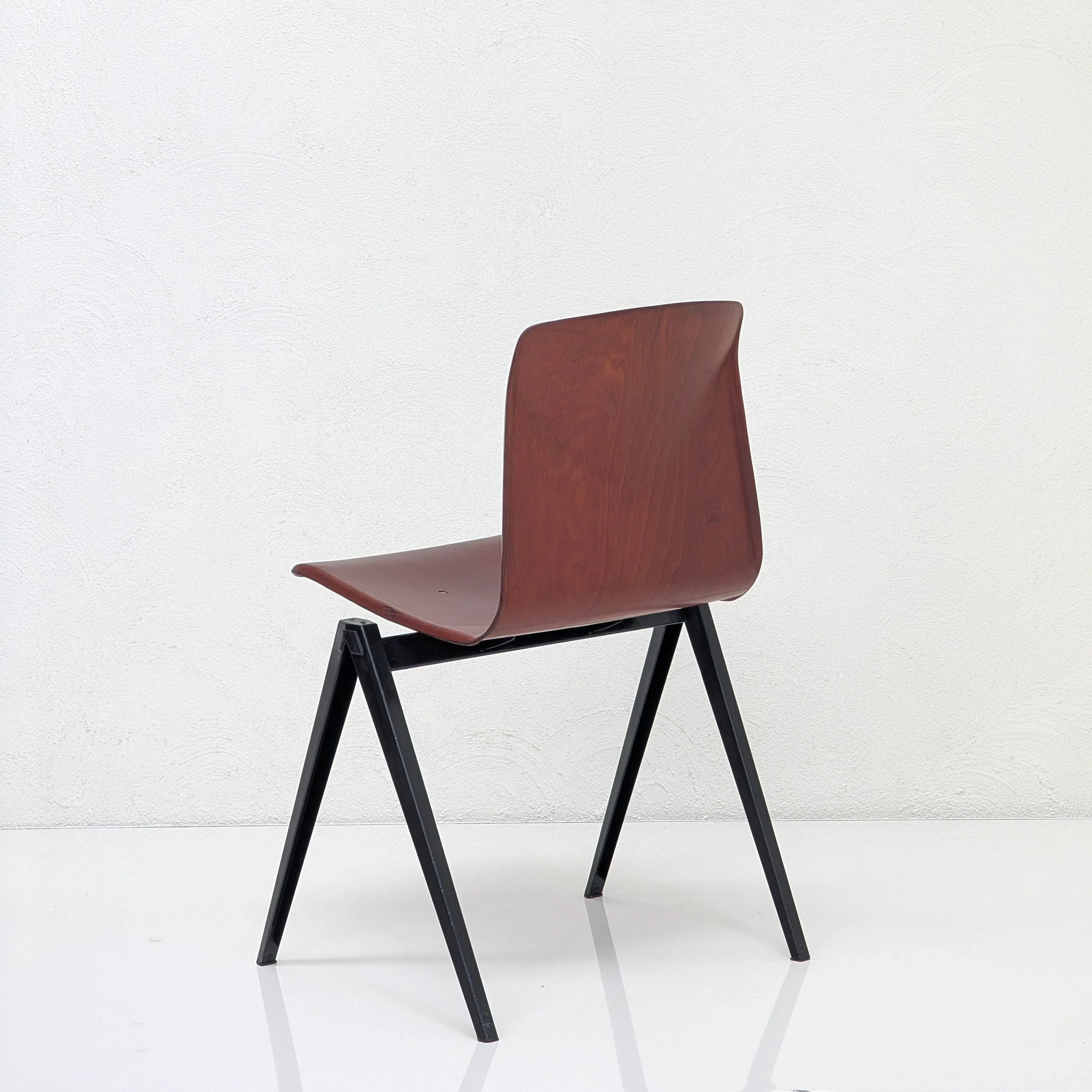 Modern chair with wooden seat and backrest, black metal legs against white textured wall