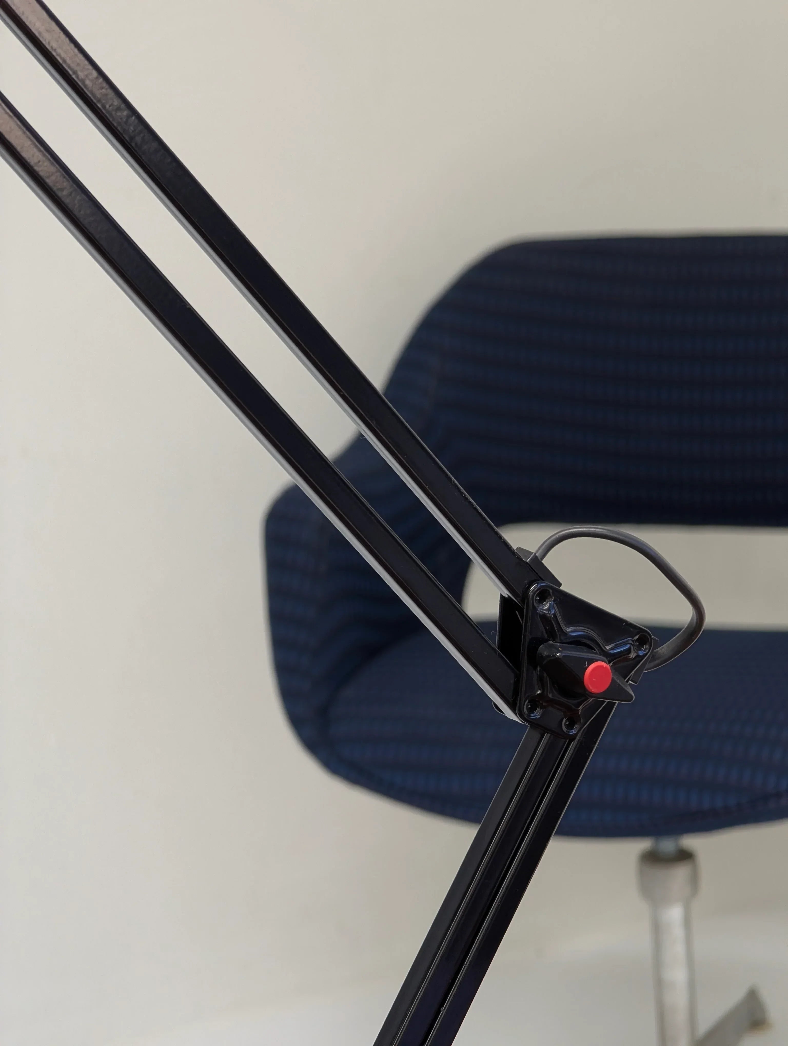 Modern blue desk chair and black metal lamp arm with red button detail in office setting