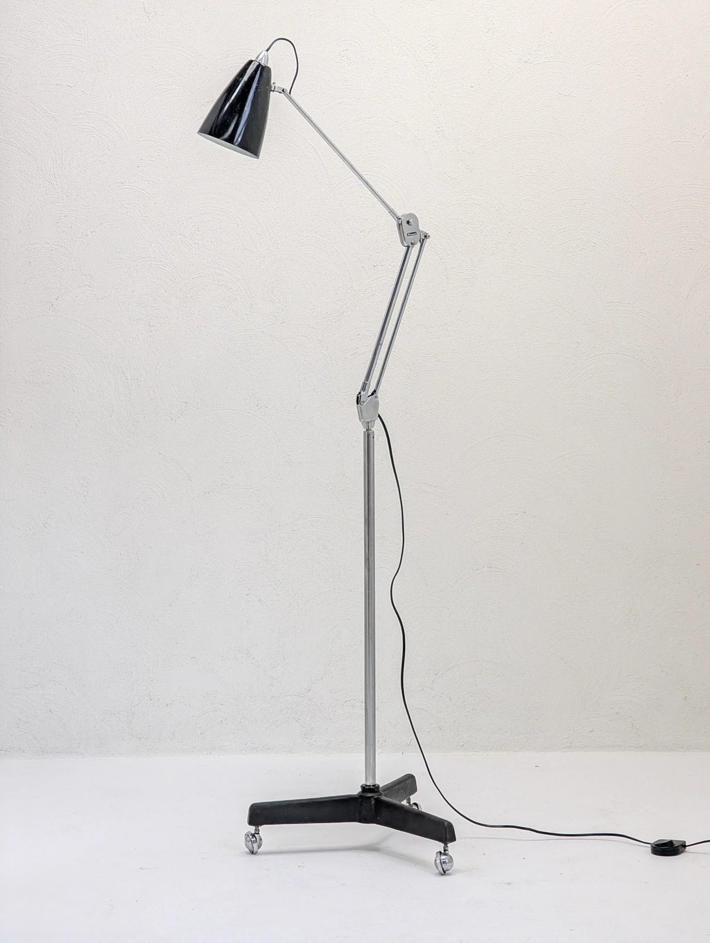 Adjustable black and chrome floor lamp on wheels against a plain white wall