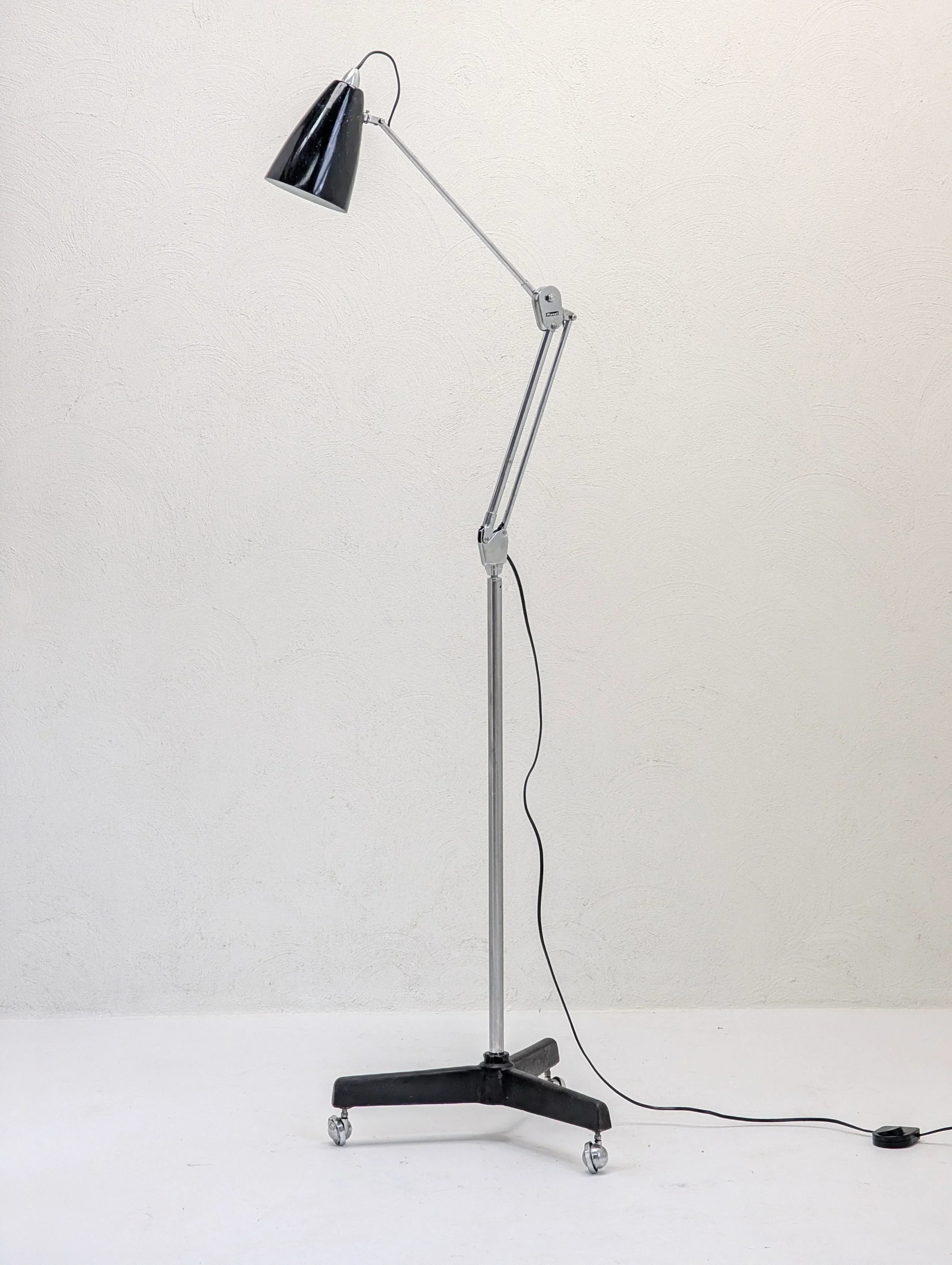 Adjustable black and chrome floor lamp on wheels against a plain white wall