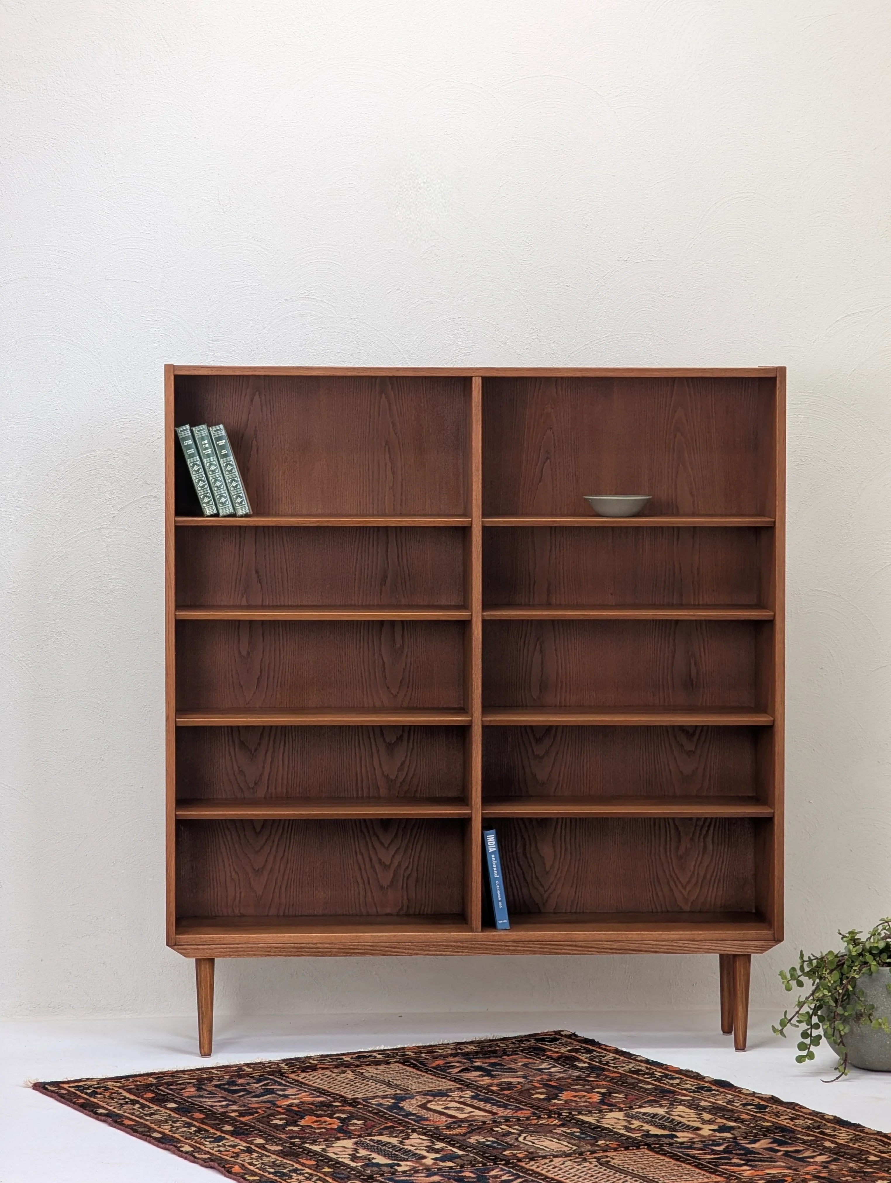 Mid-century modern wooden bookshelf with minimal decor, placed on a patterned rug with white textured wall background