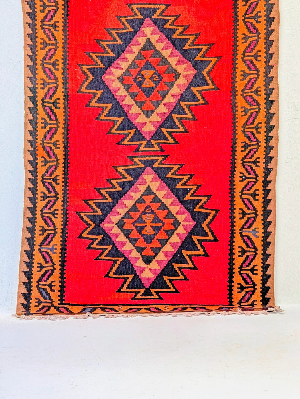 Vintage kilim rug with geometric diamond pattern in red, black, and orange on a white floor