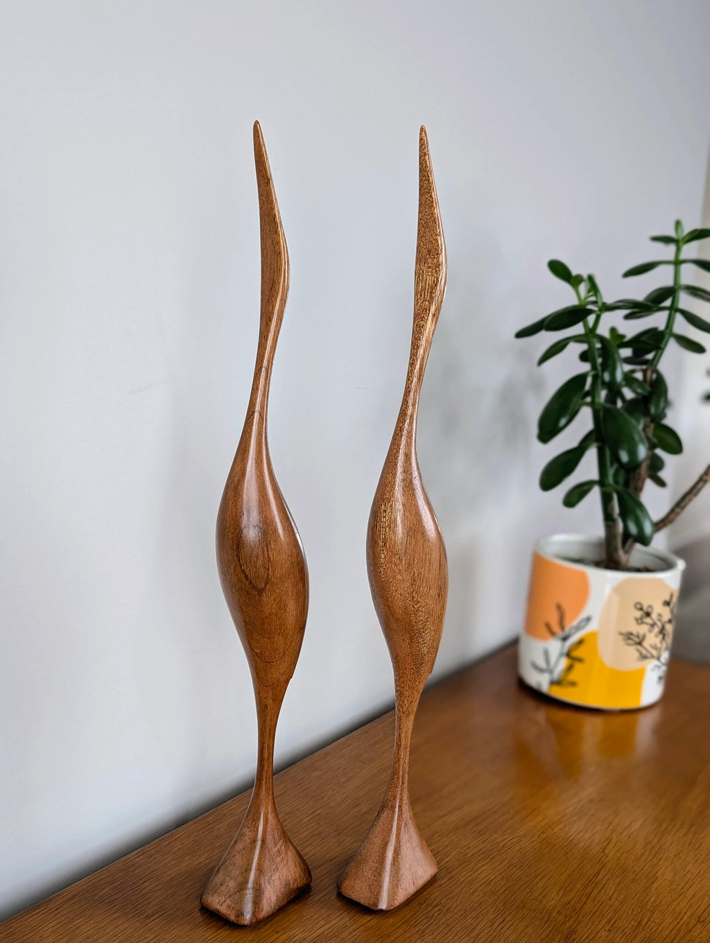 Pair of tall wooden bird sculptures on wooden table with potted plant in colorful pot