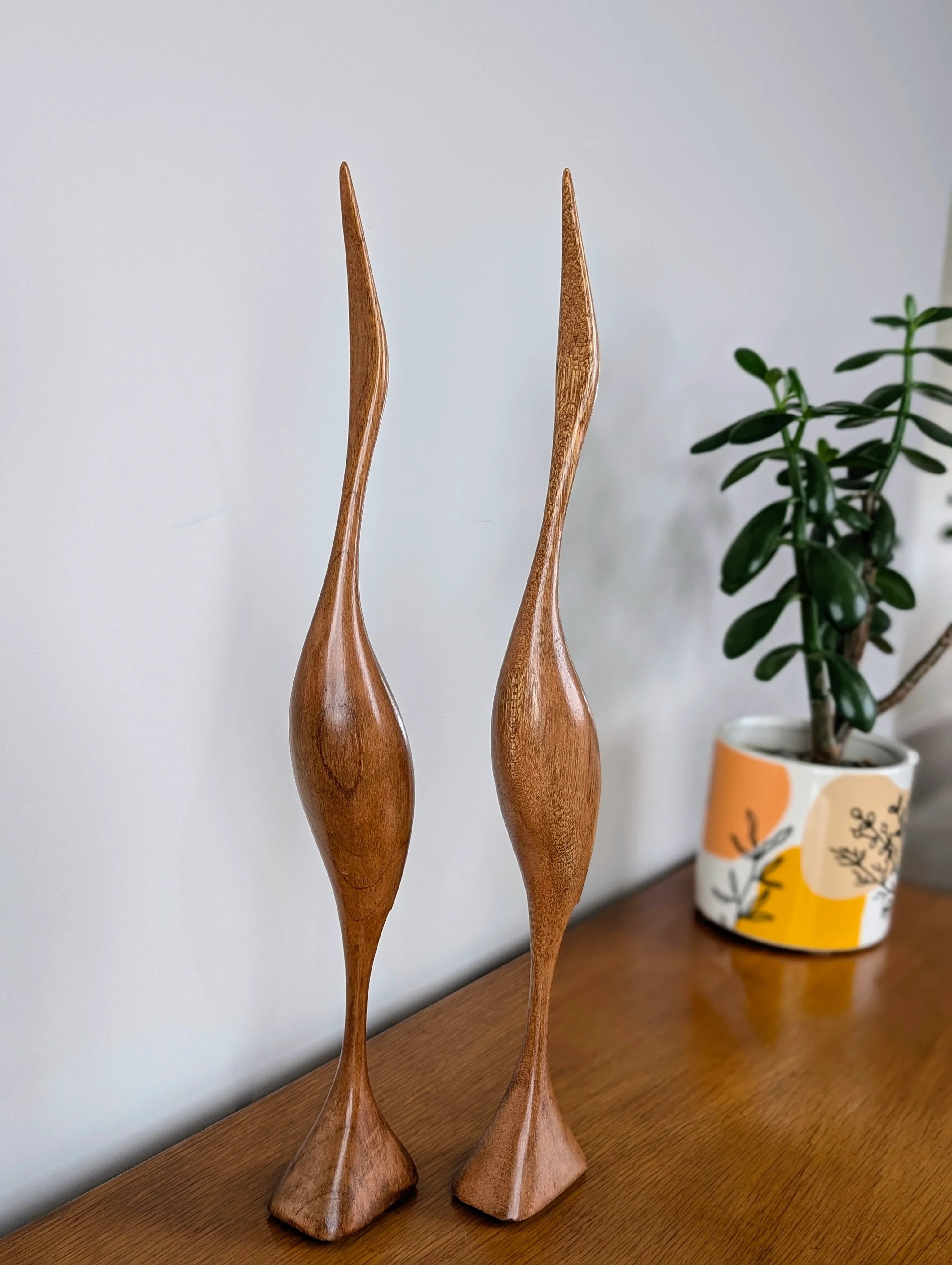 Pair of tall wooden bird sculptures on wooden table with potted plant in colorful pot
