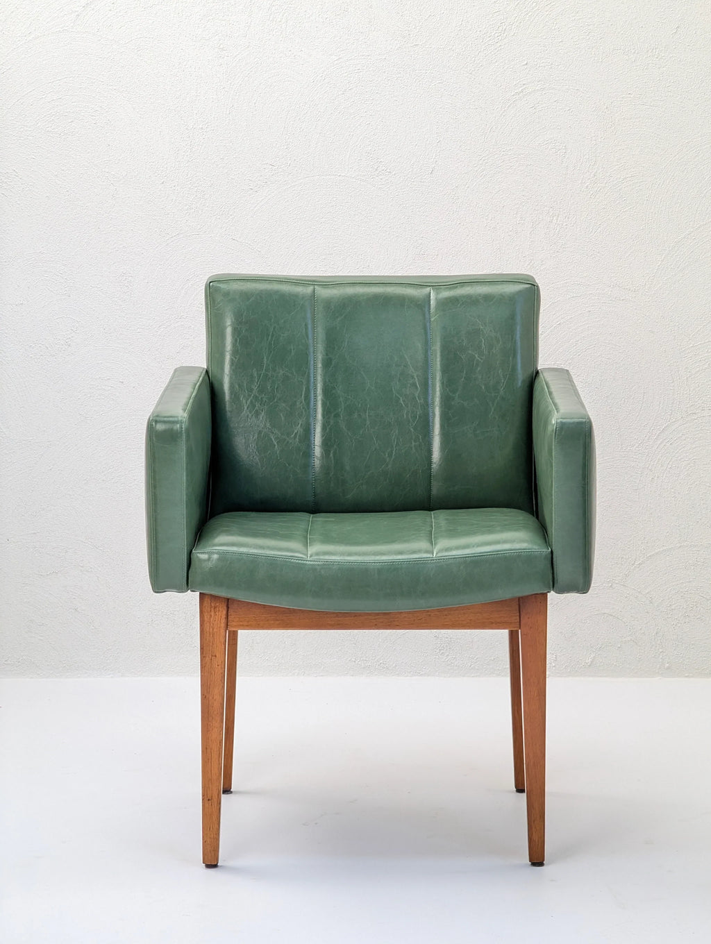 Mid-century modern green leather armchair with wooden legs against a white wall