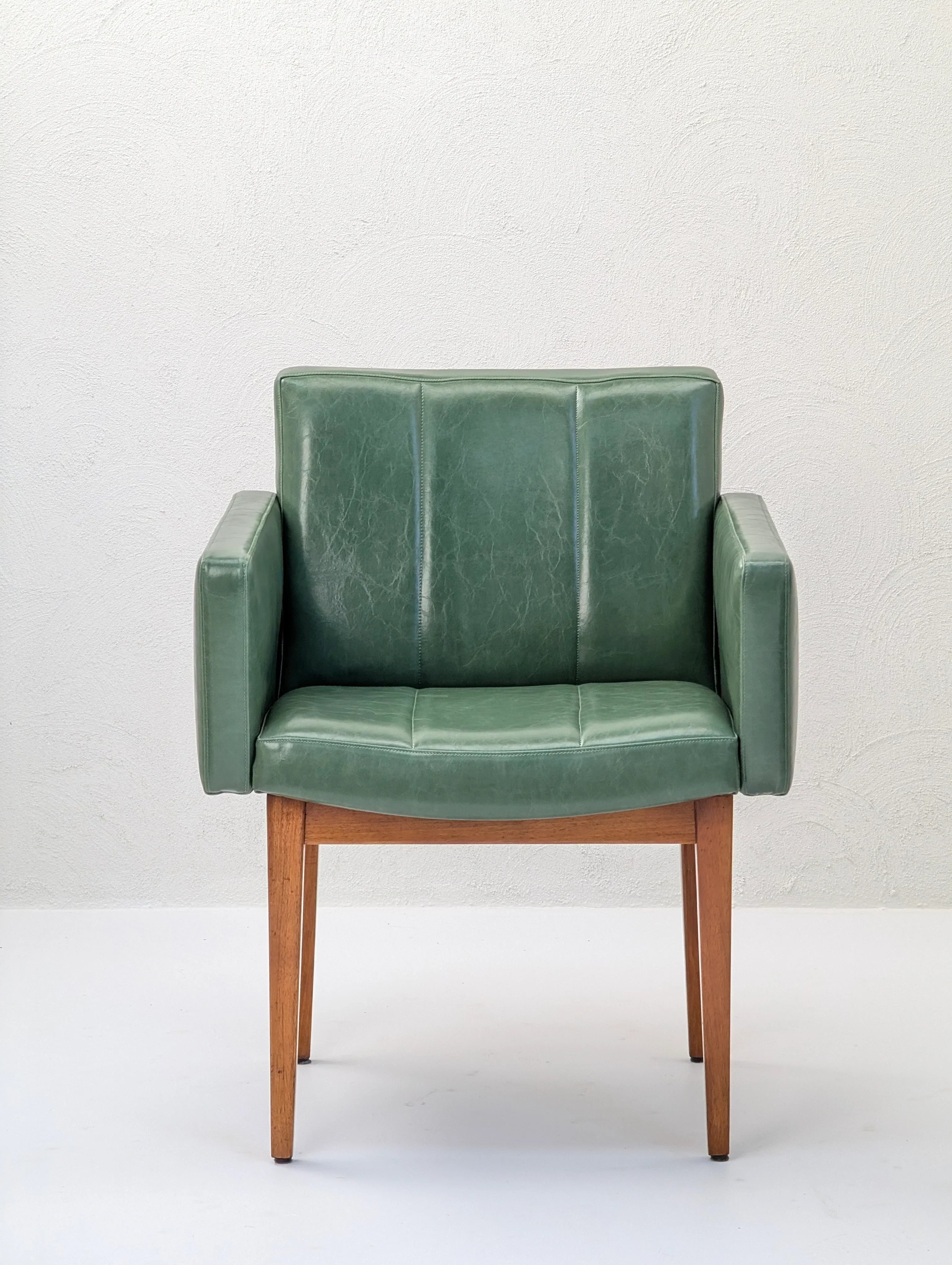 Mid-century modern green leather armchair with wooden legs against a white wall