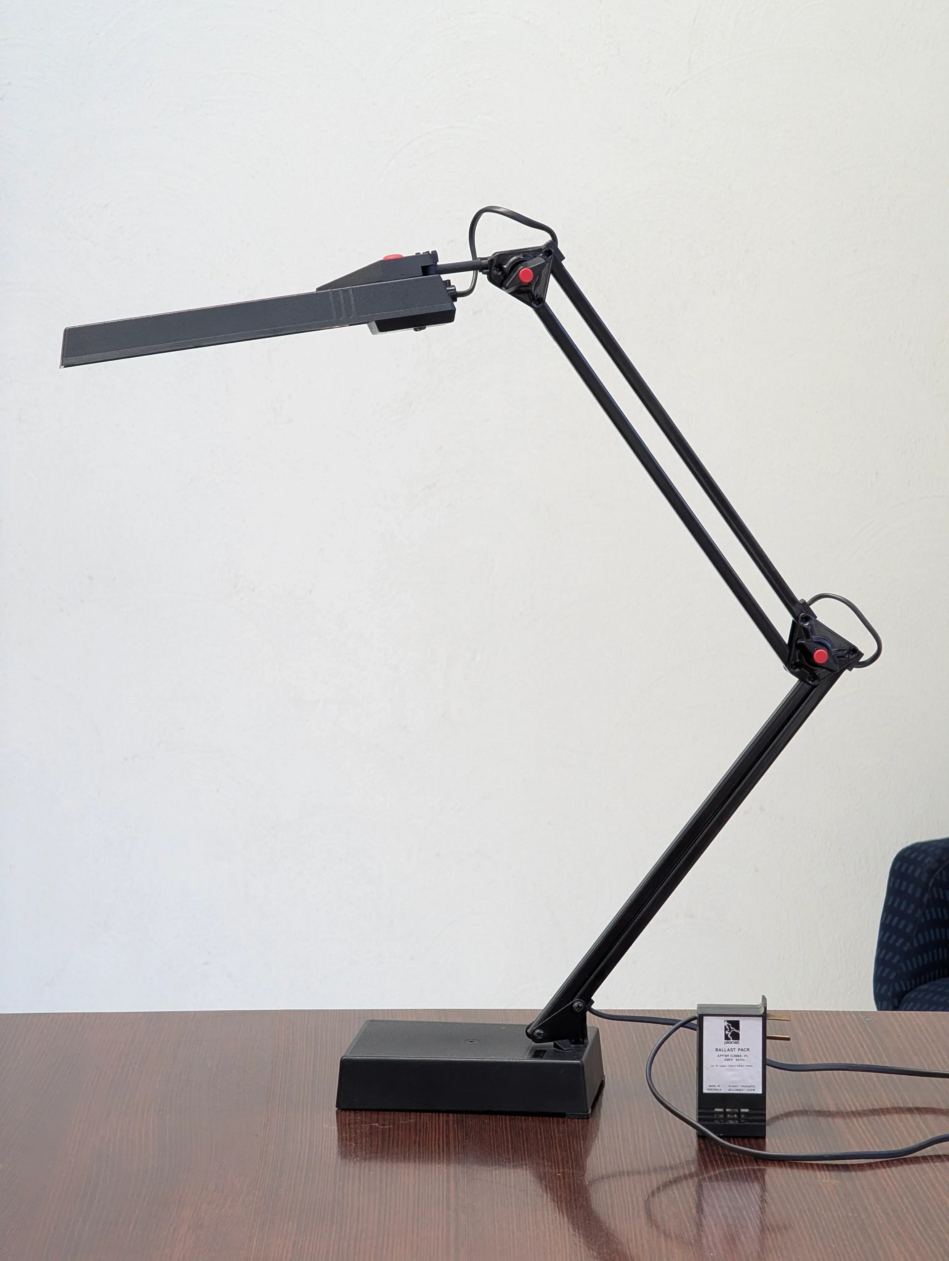 Modern black adjustable desk lamp with power adapter on wooden table against a white wall