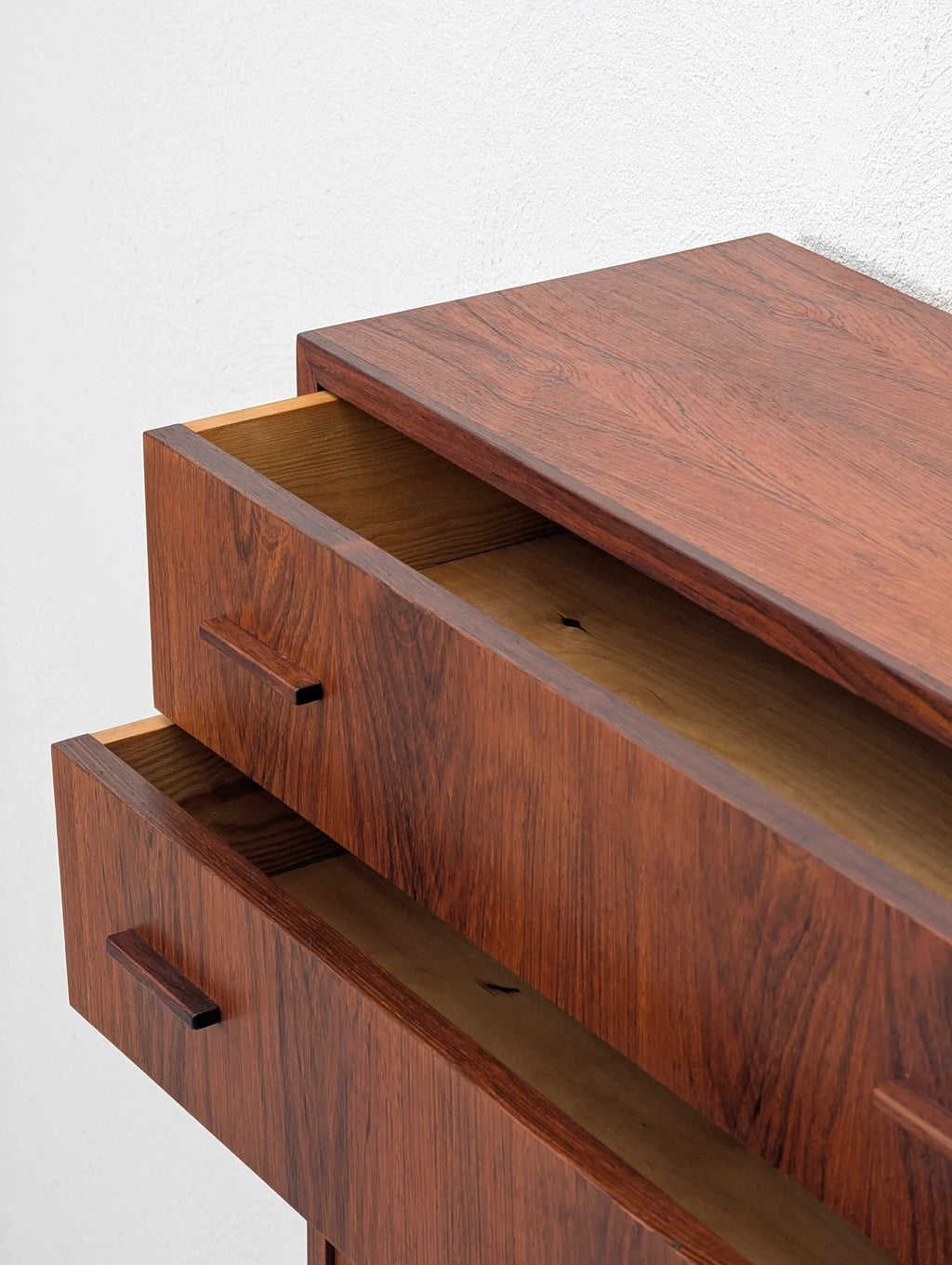 Mid-century modern wood dresser with two open drawers against a white wall