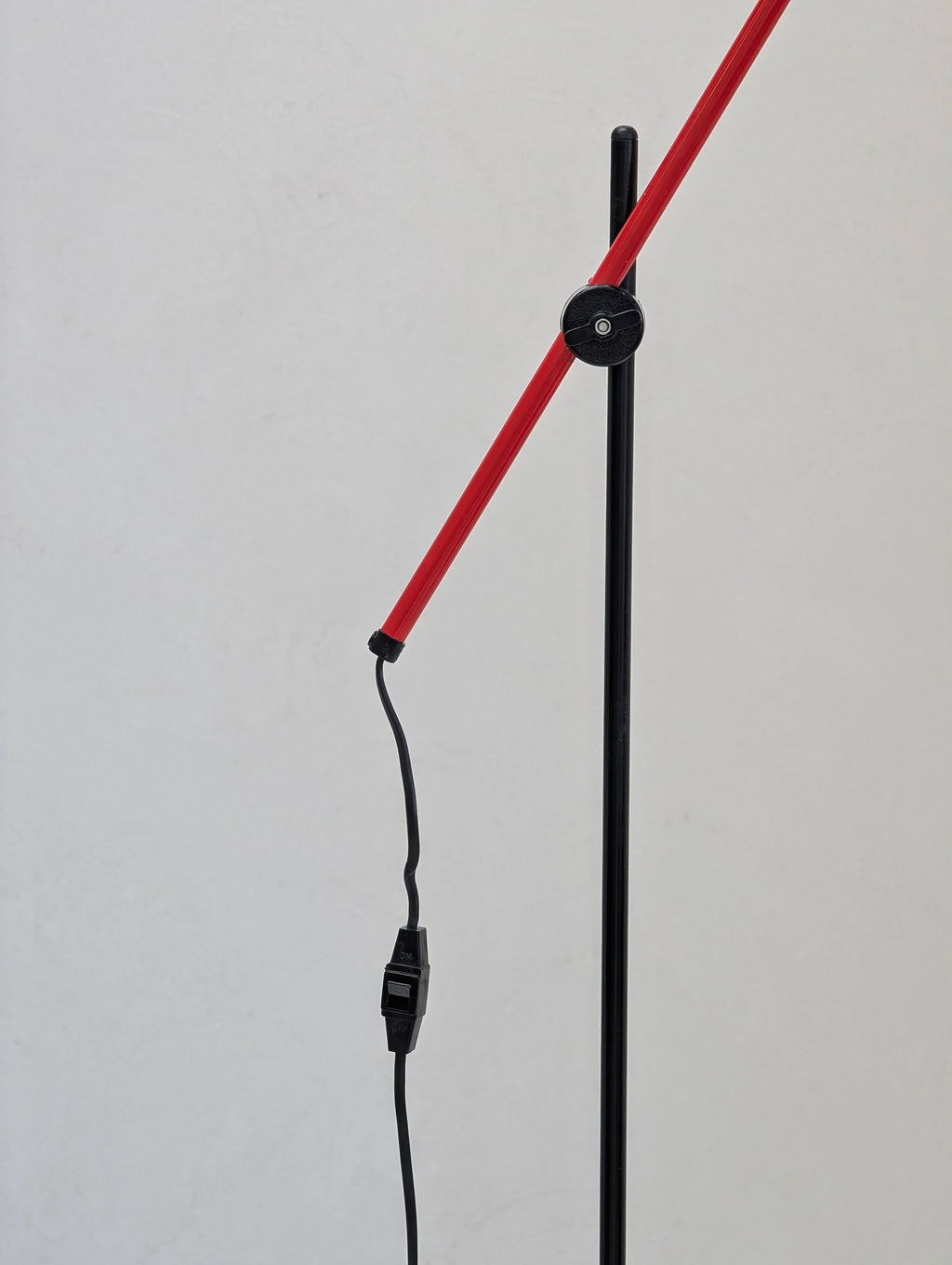 Modern red and black adjustable lamp with cord and switch against plain wall