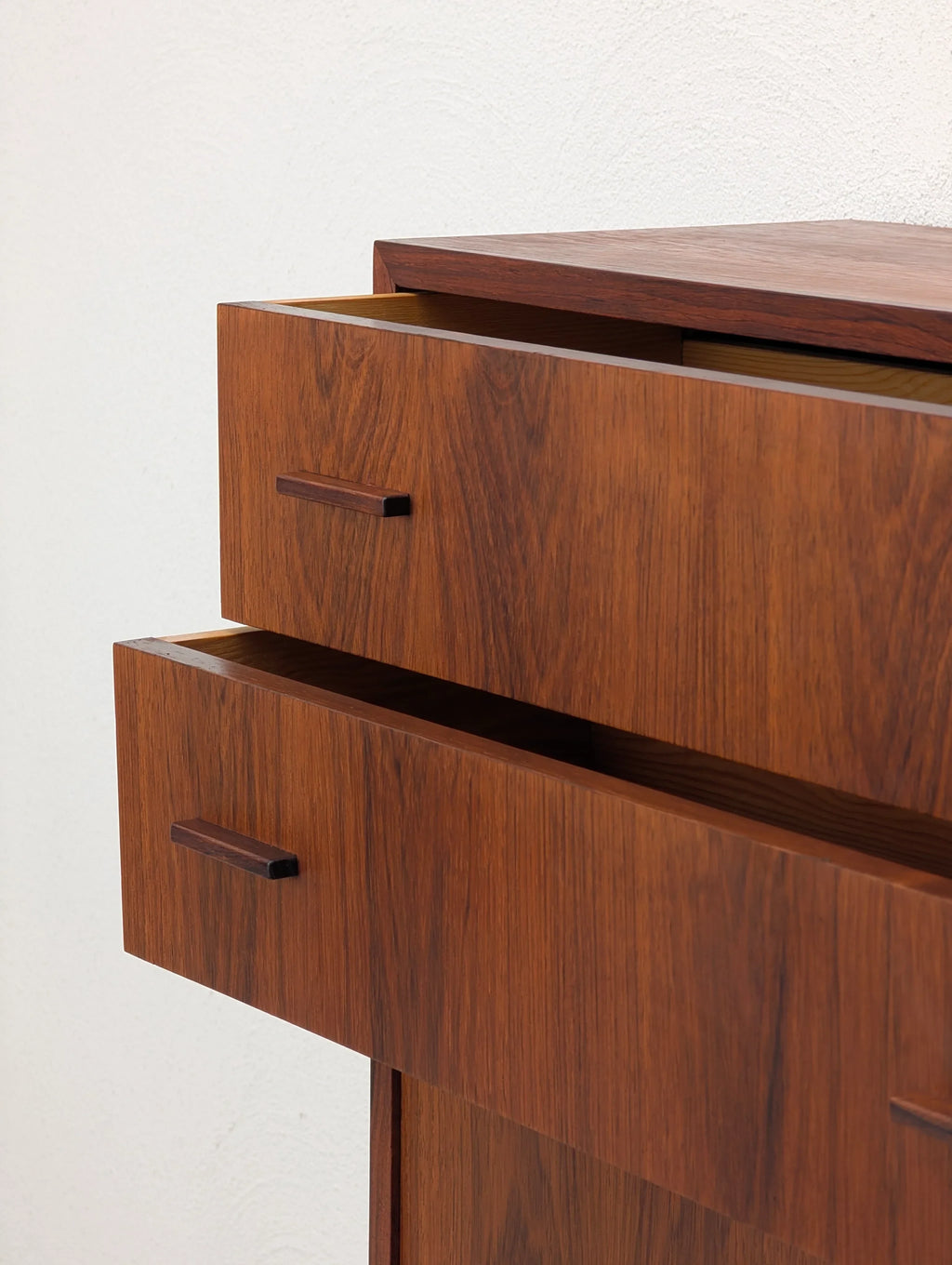 Mid-century modern wooden dresser with two open drawers against a white wall