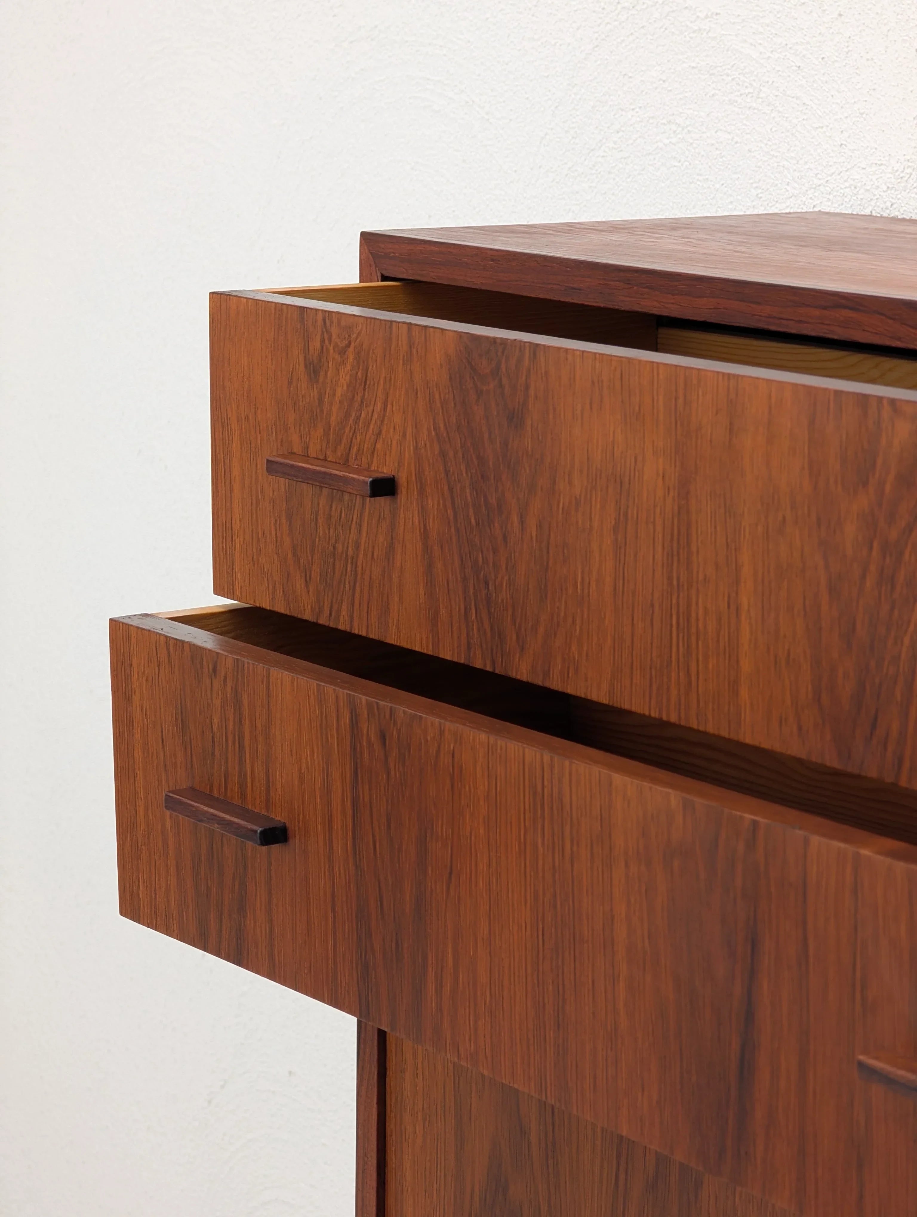 Mid-century modern wooden dresser with two open drawers against a white wall