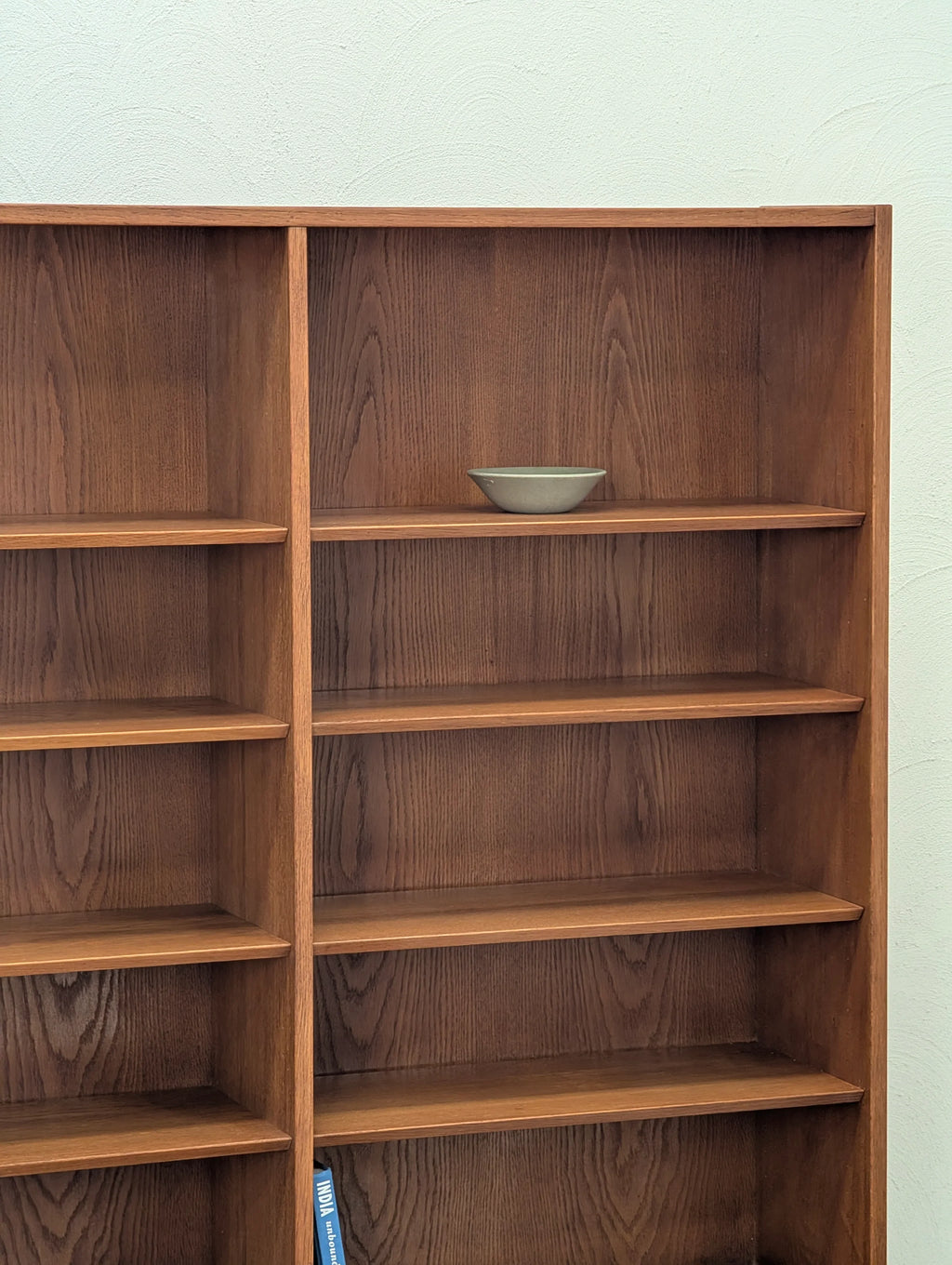 Empty wooden bookshelf with dark wood finish and a small green ceramic bowl on an upper shelf
