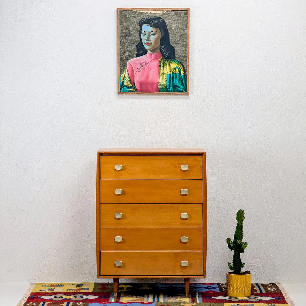 Mid-century modern wooden dresser with four drawers, cactus in yellow pot, framed portrait above