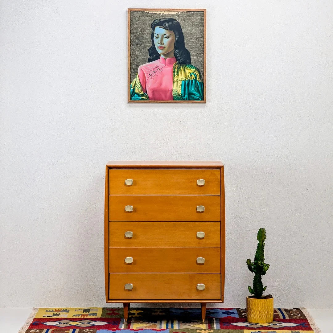 Mid-century modern wooden dresser with four drawers, cactus in yellow pot, framed portrait above