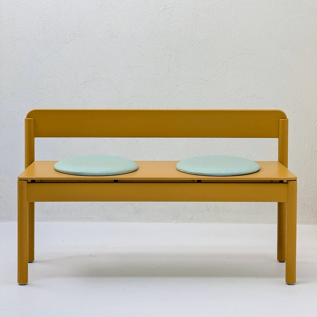 Minimalist yellow bench with two round light blue seat cushions against a white wall
