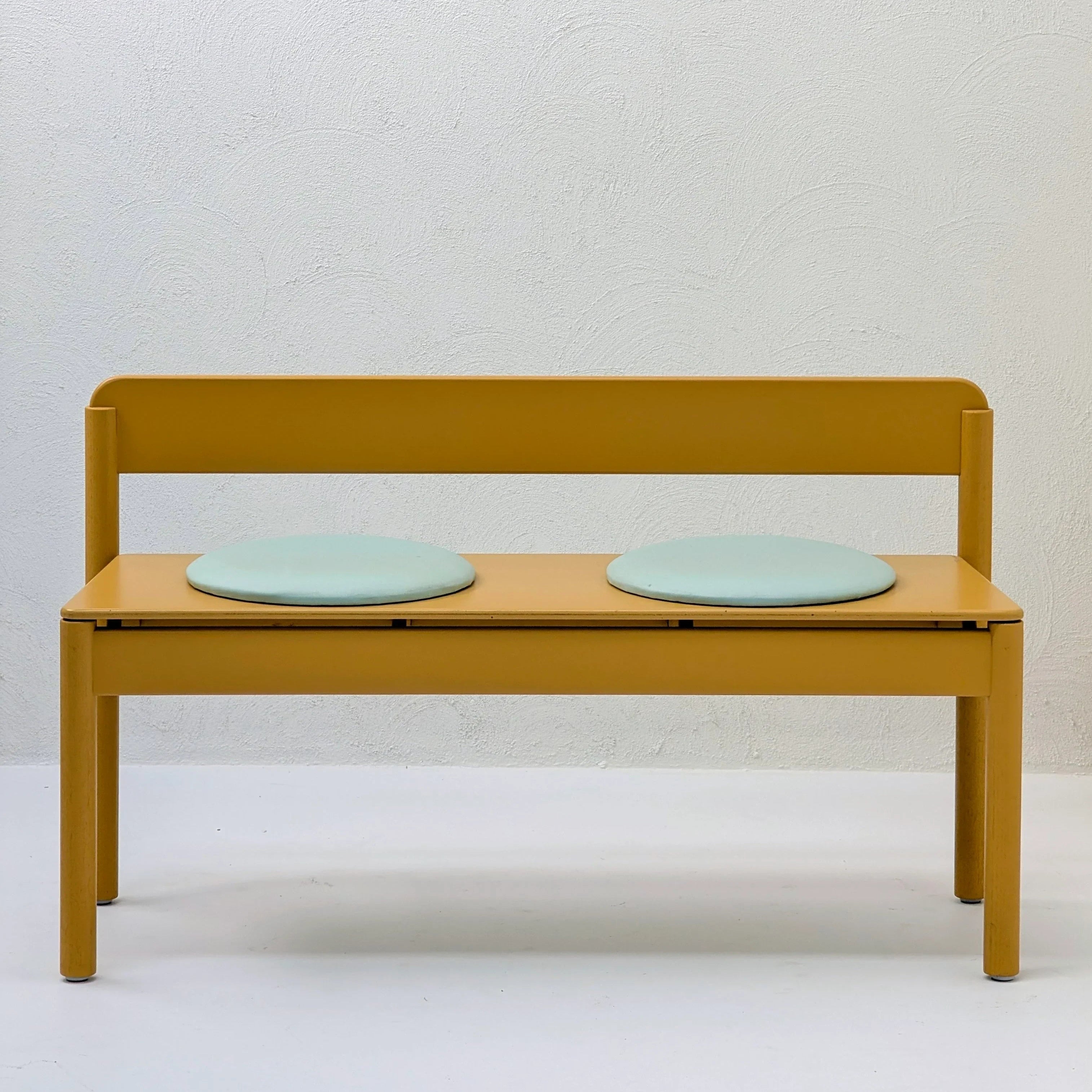 Minimalist yellow bench with two round light blue seat cushions against a white wall