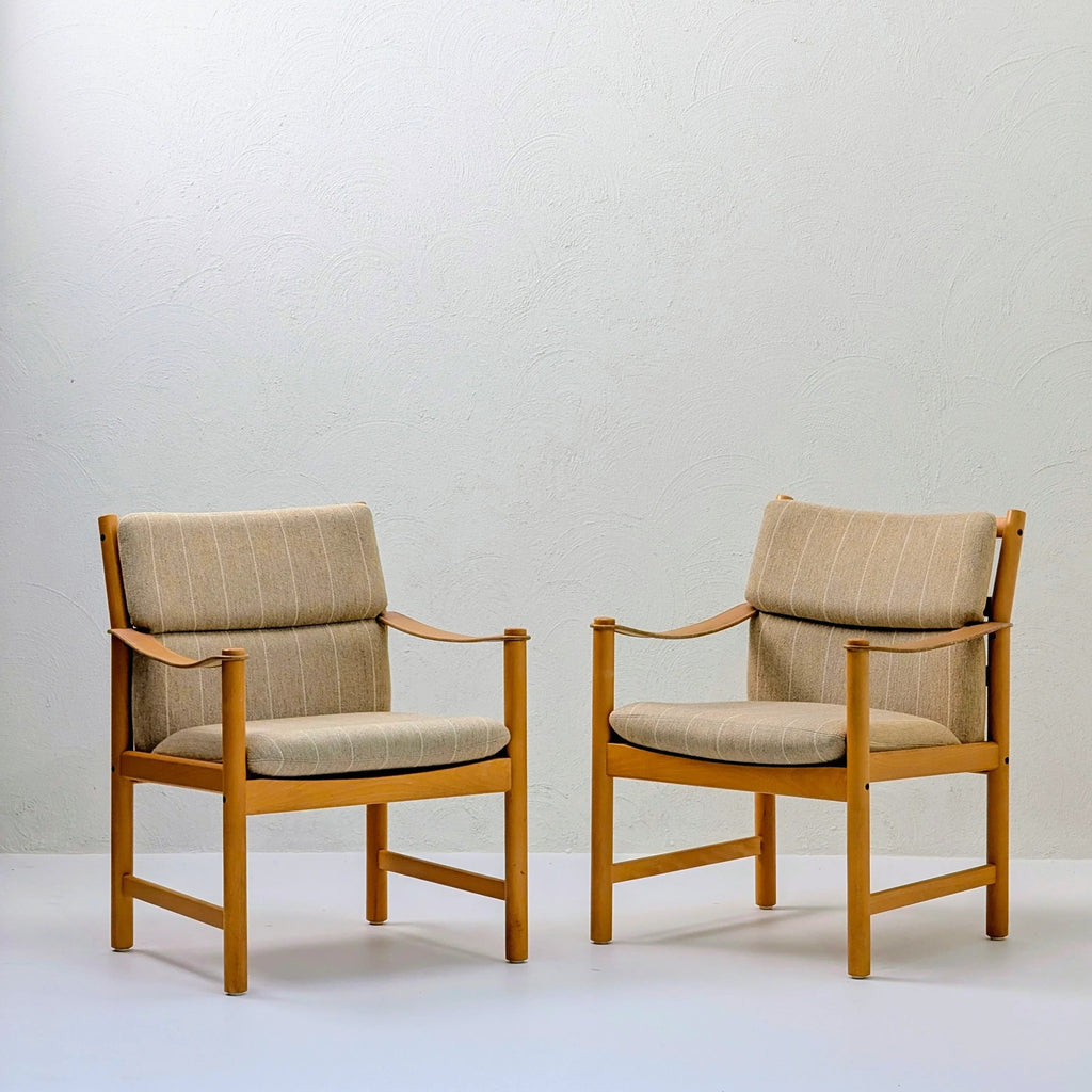 Pair of modern wooden armchairs with beige striped cushions against a white wall