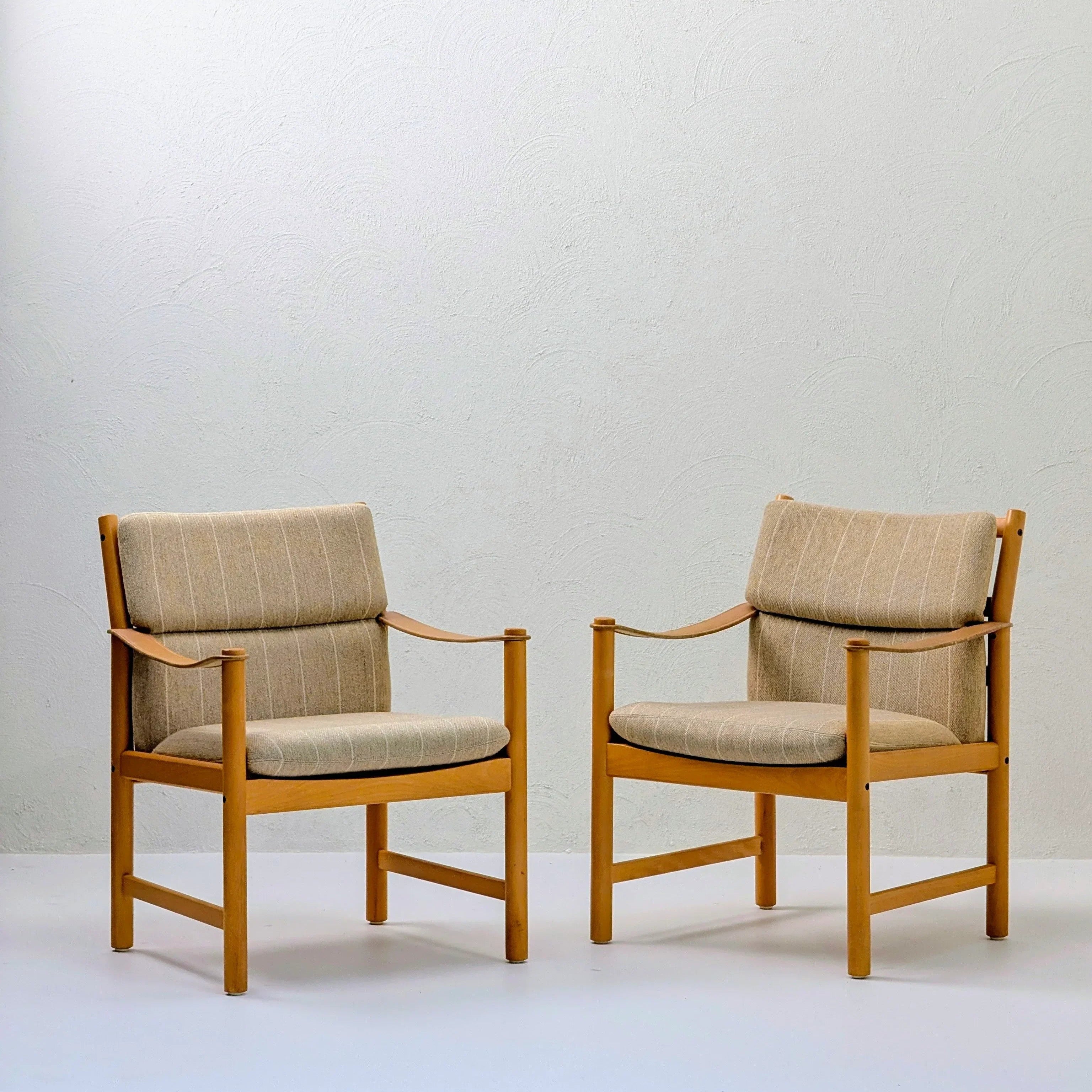 Pair of modern wooden armchairs with beige striped cushions against a white wall