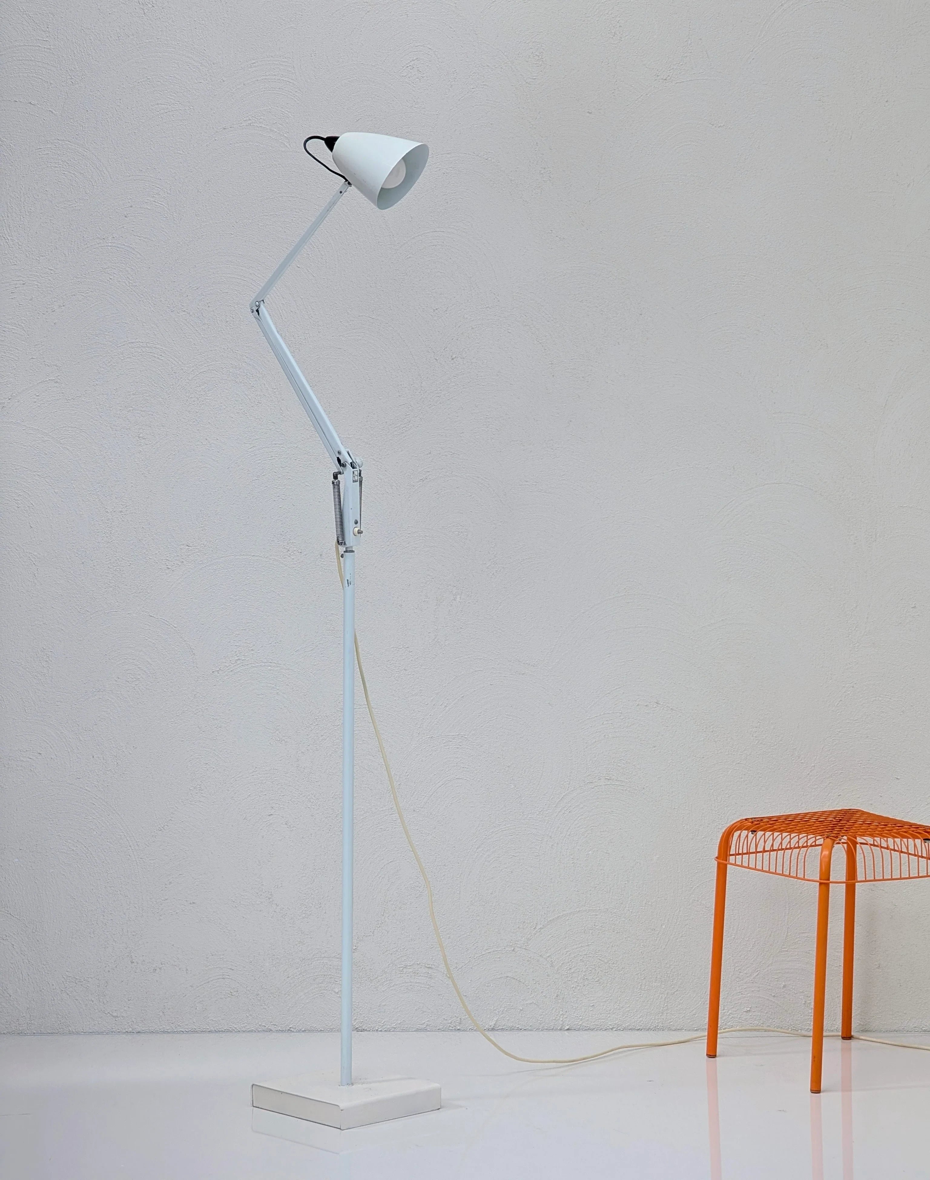 Minimalist white adjustable floor lamp next to an orange metal wire stool on a white floor
