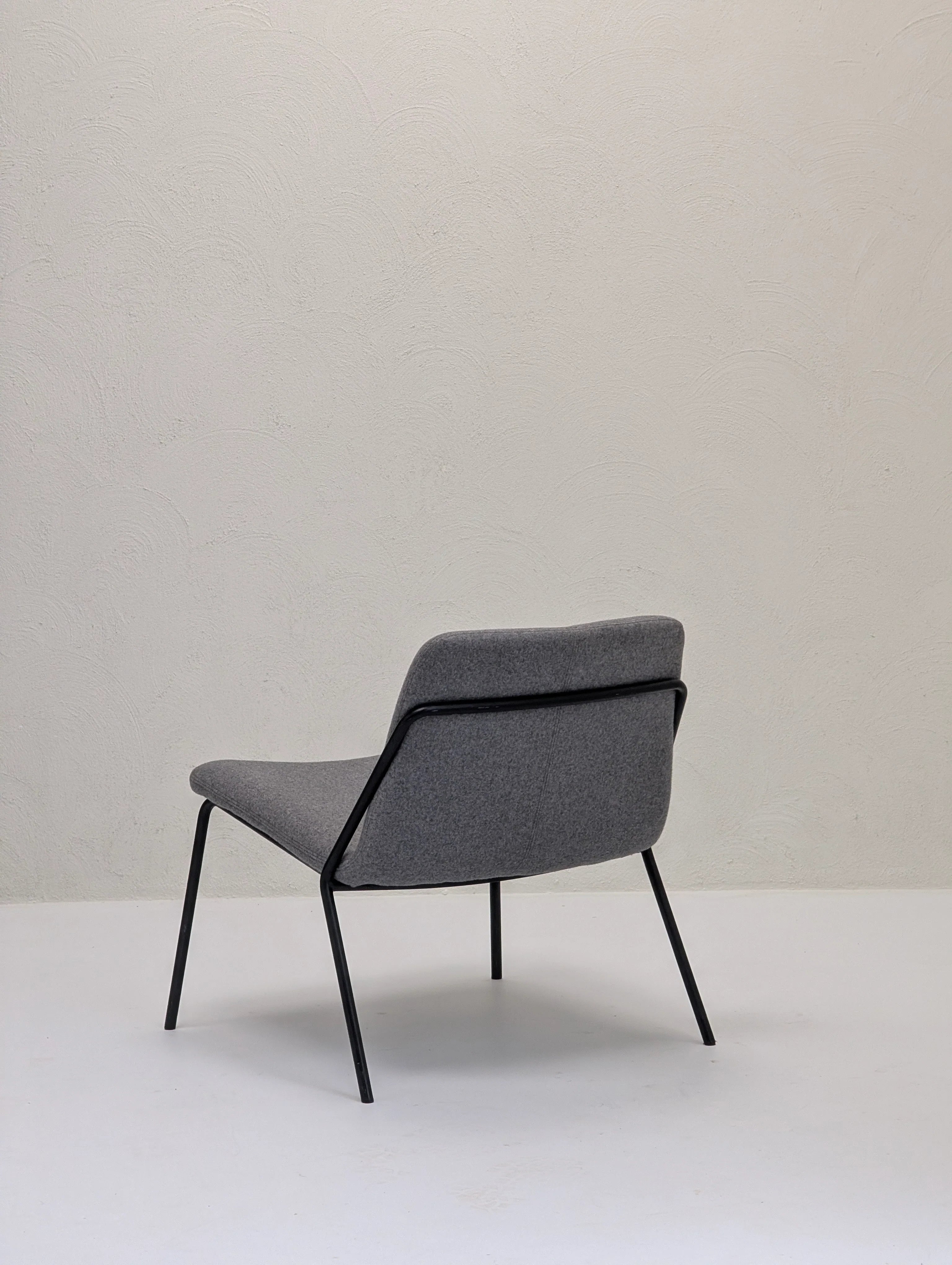 Minimalist grey fabric lounge chair with black metal legs on white floor against textured light wall