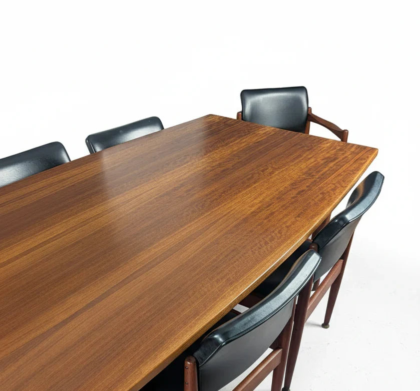 Mid-century modern wooden dining table with six black leather chairs on white background