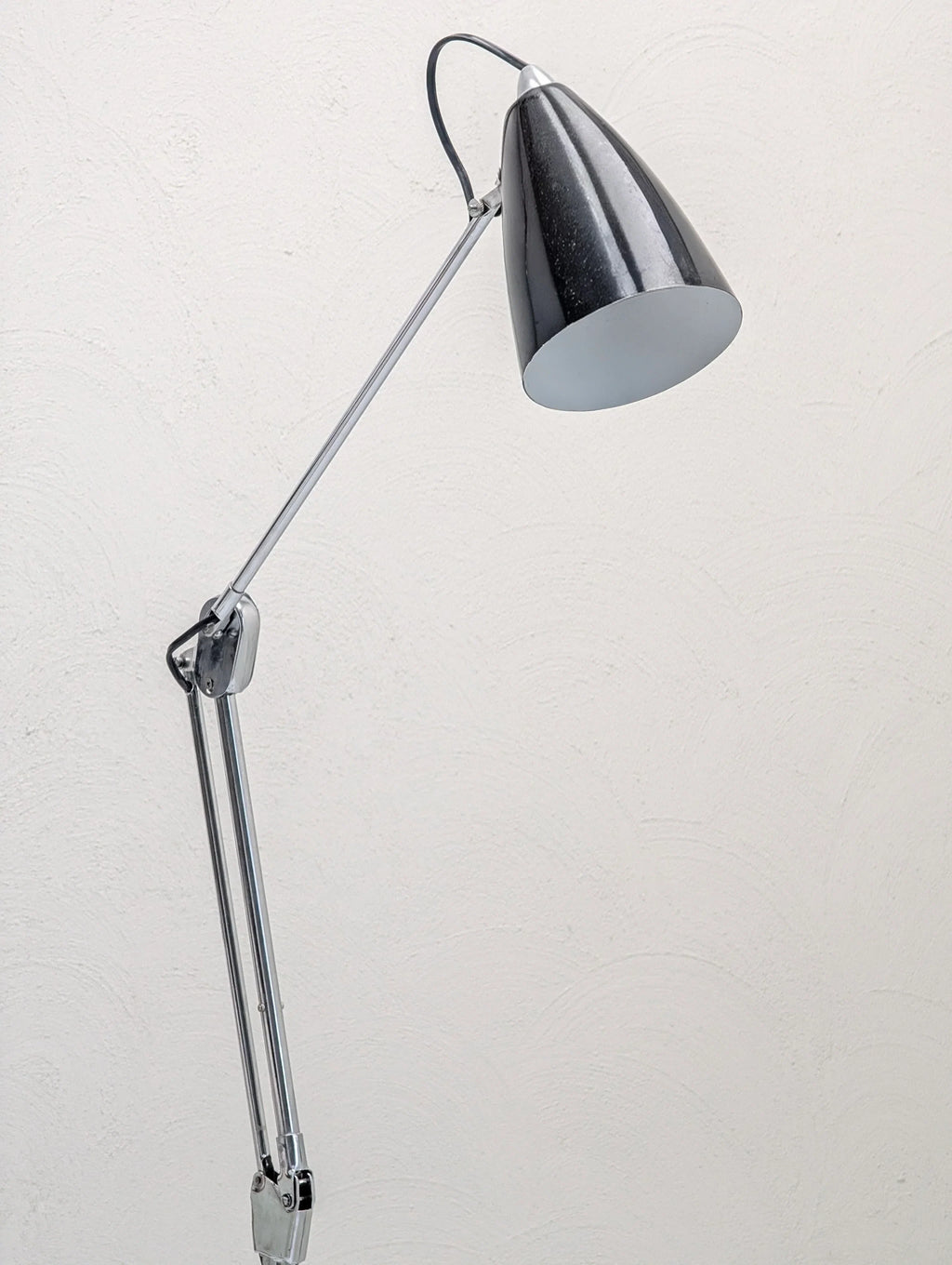 Modern adjustable desk lamp with chrome arm against a textured white wall