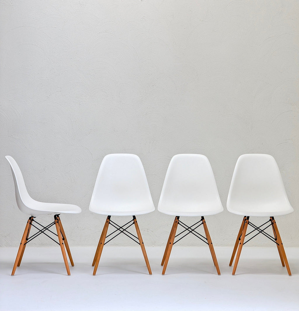 Four white modern chairs with wooden legs against a textured light gray wall