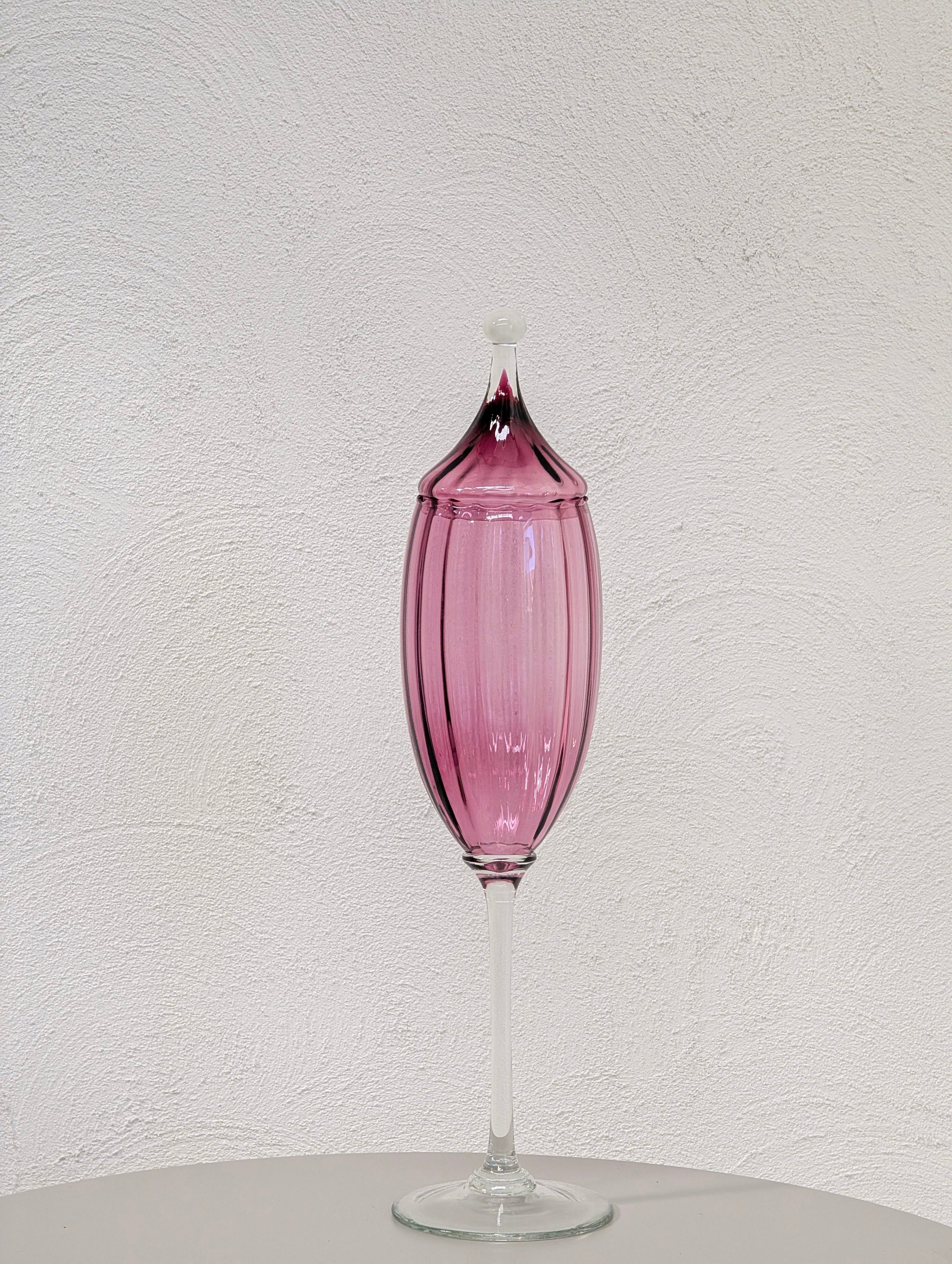 Tall decorative purple glass vase with a lid on a white textured wall background