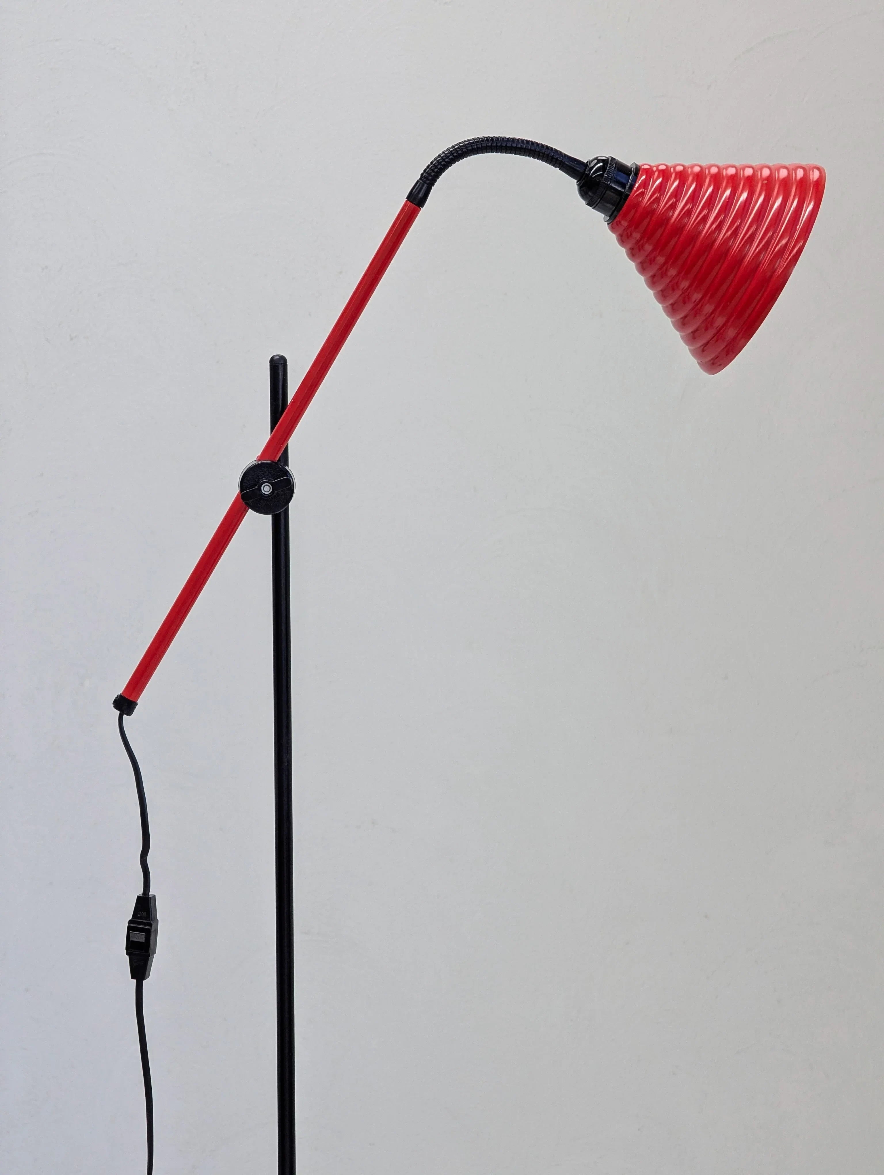 Modern adjustable red floor lamp with spiral lampshade against plain white wall