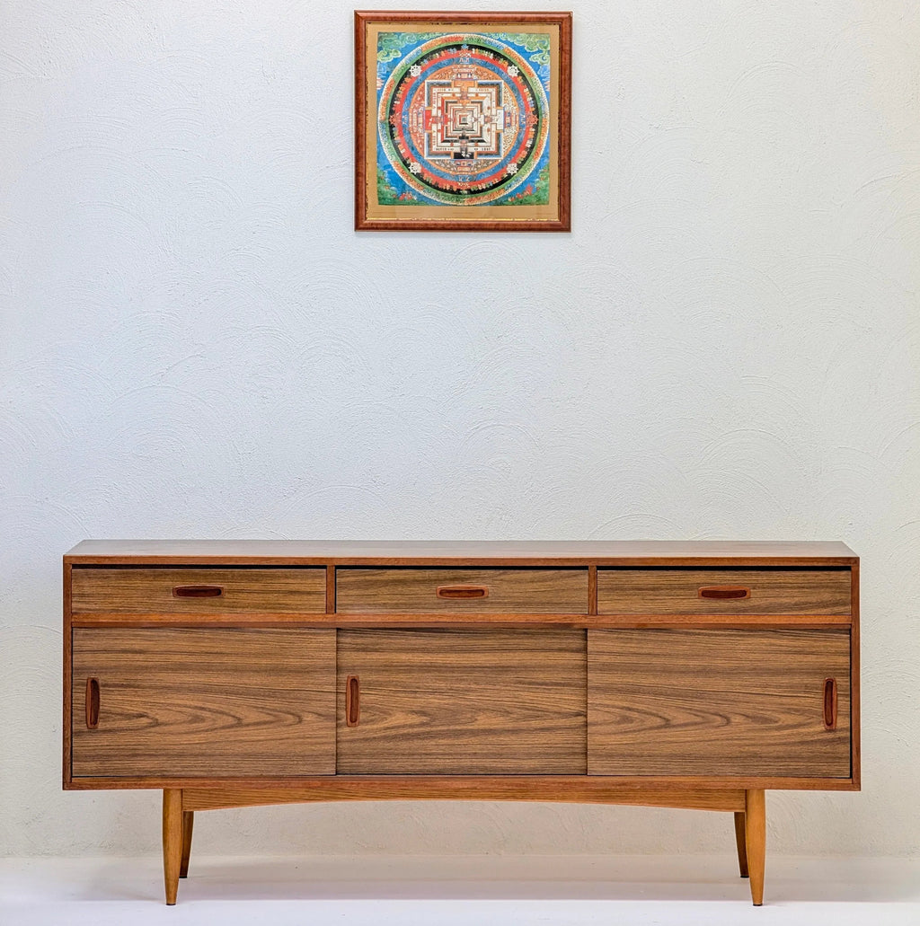 Mid-century modern wooden sideboard with three drawers and sliding doors below, light background