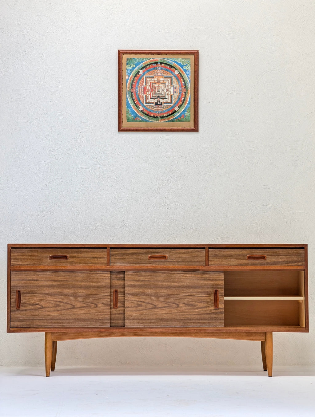 Mid-century modern wooden sideboard with sliding doors and three drawers under framed colorful circular art