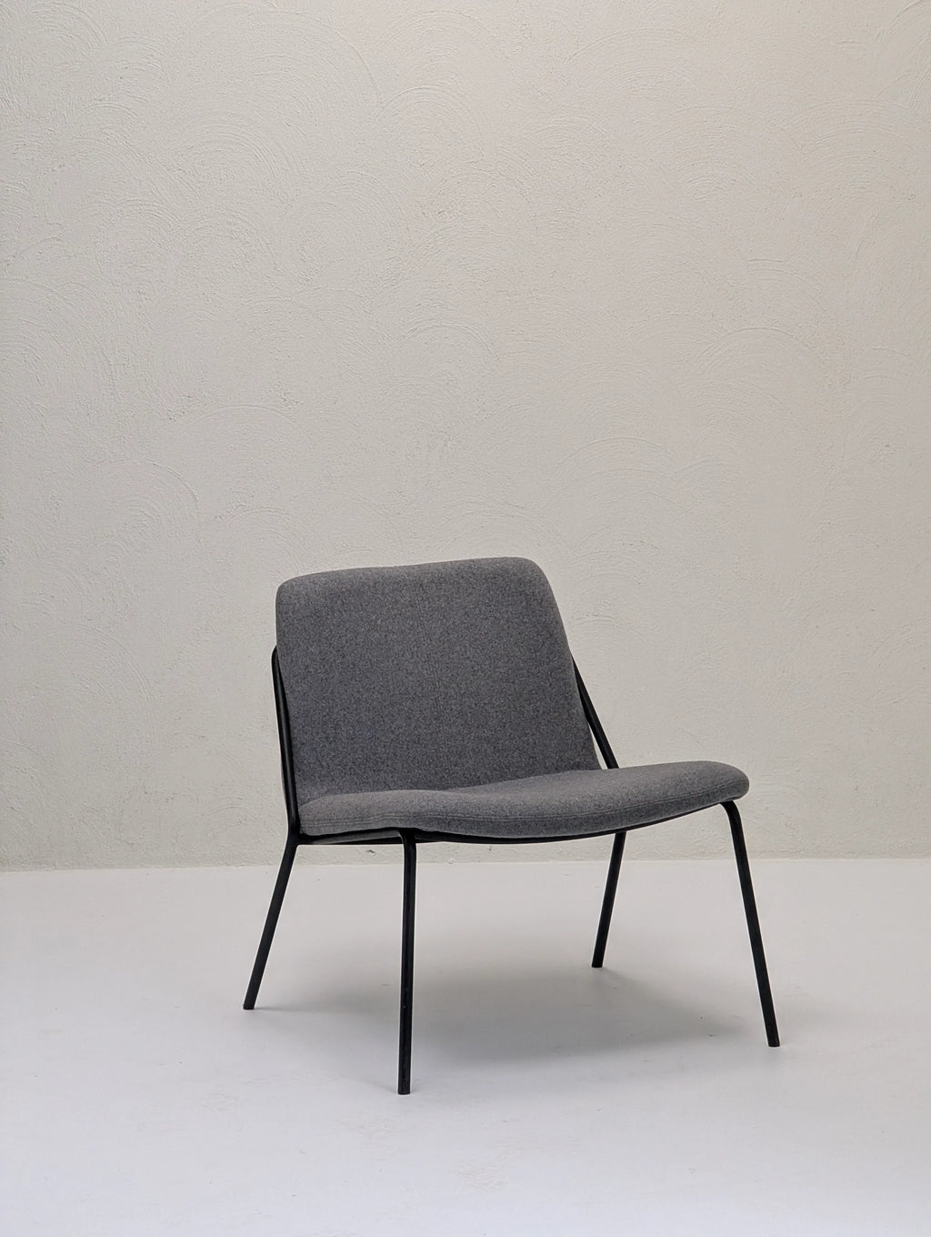 Modern gray fabric lounge chair with black metal legs against textured beige wall