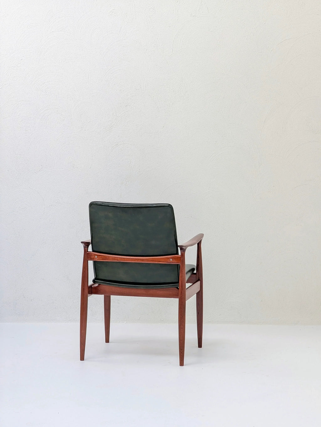 Mid-century modern wooden chair with dark green leather backrest in minimal white room