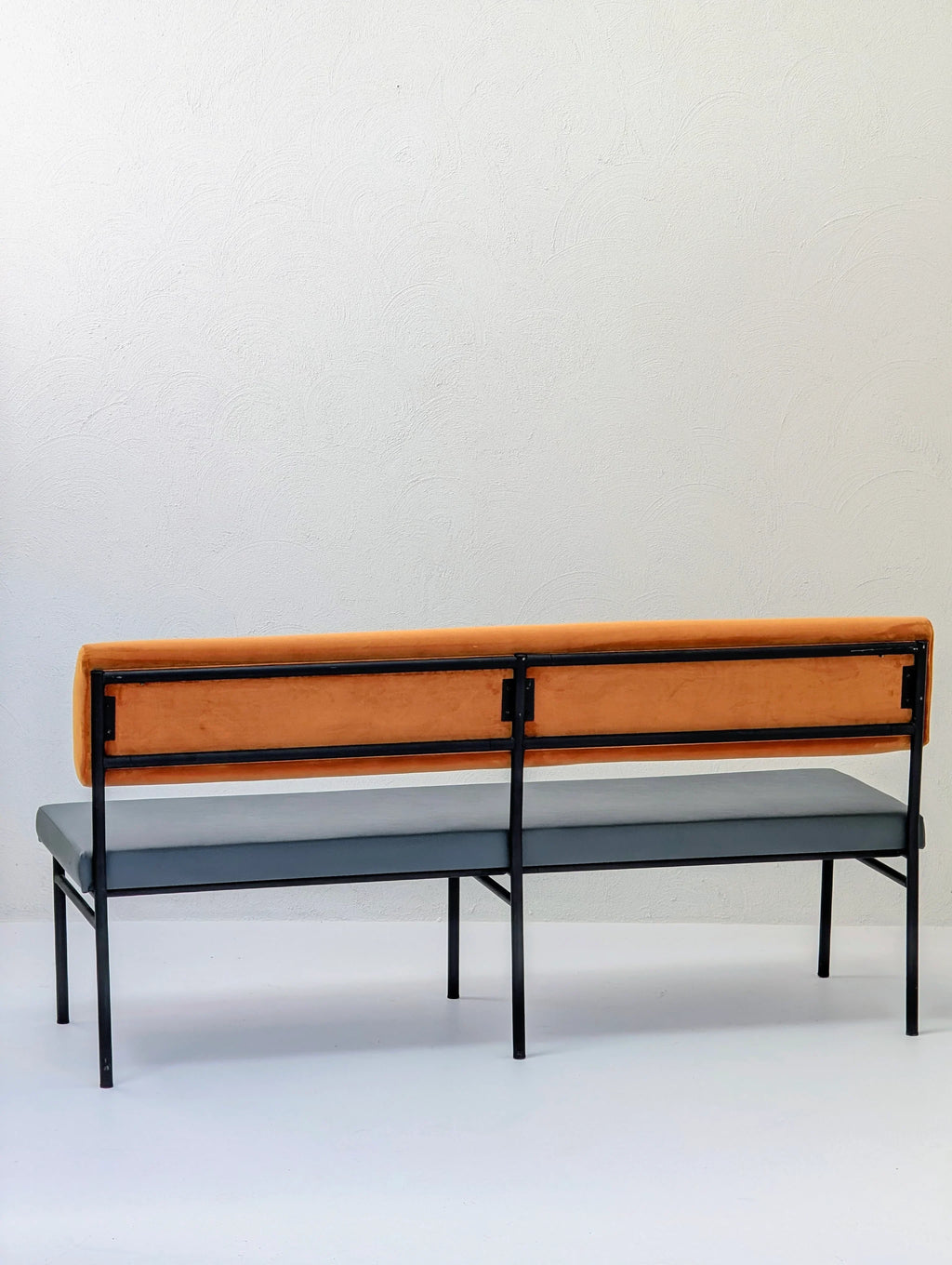 Modern bench with orange backrest, gray seat, and black metal frame against white wall